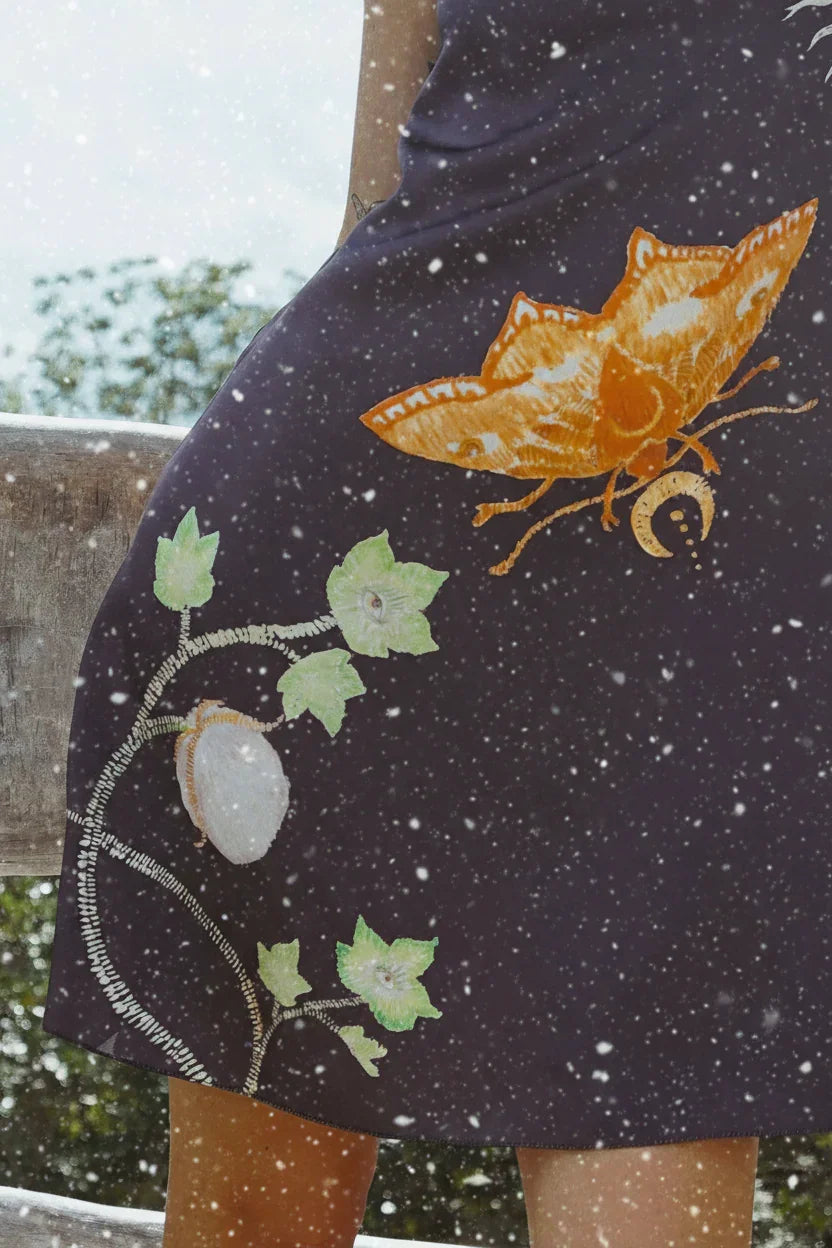 Close-up of black skirt with orange butterfly and green leaf embroidery in outdoor setting with falling snow