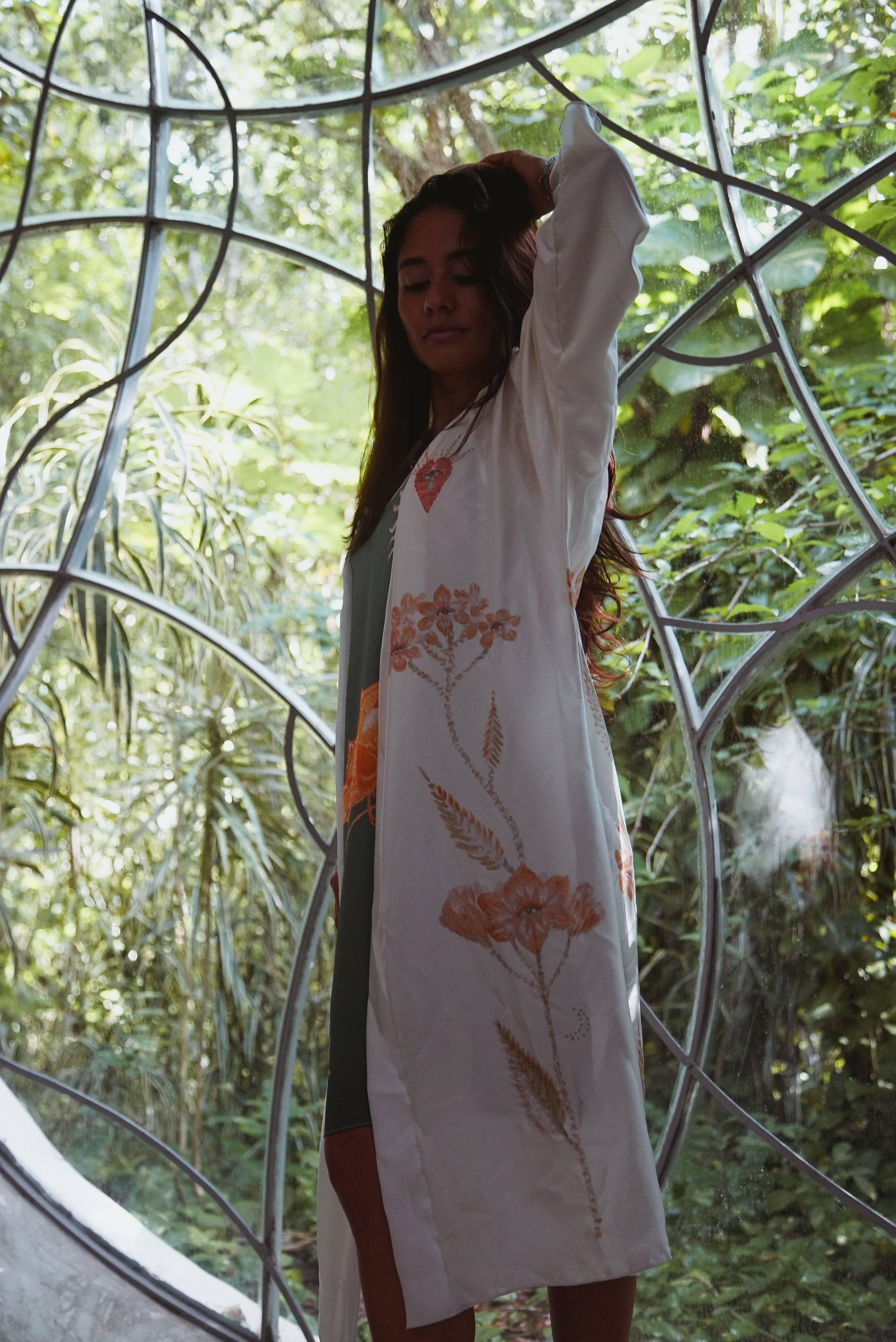 Woman in floral white robe standing inside geometric glass greenhouse surrounded by lush greenery