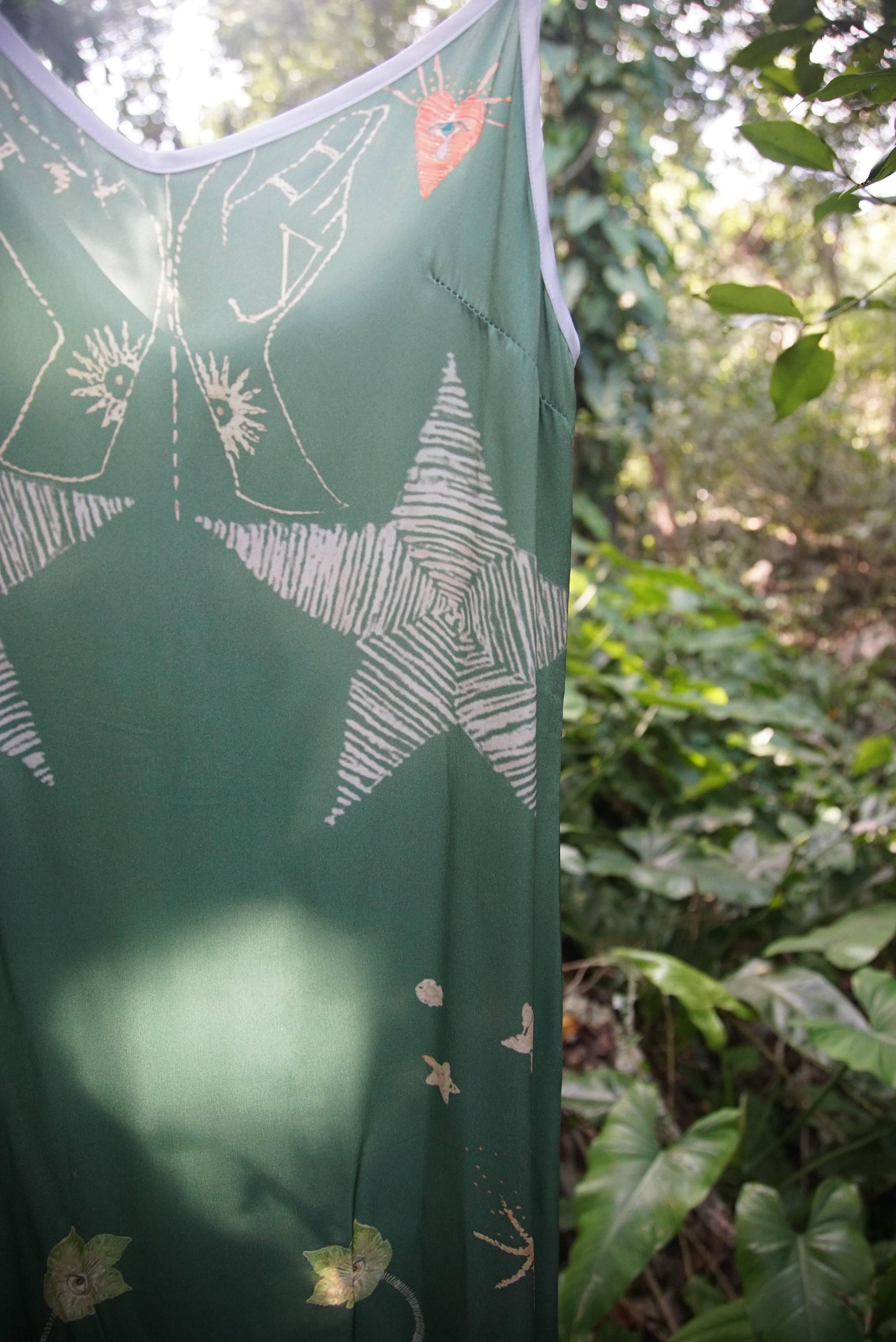 Green dress with white star and hand print patterns hanging outdoors amid lush green foliage
