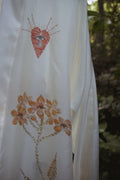White fabric with hand-painted orange heart and floral designs against a blurred natural background