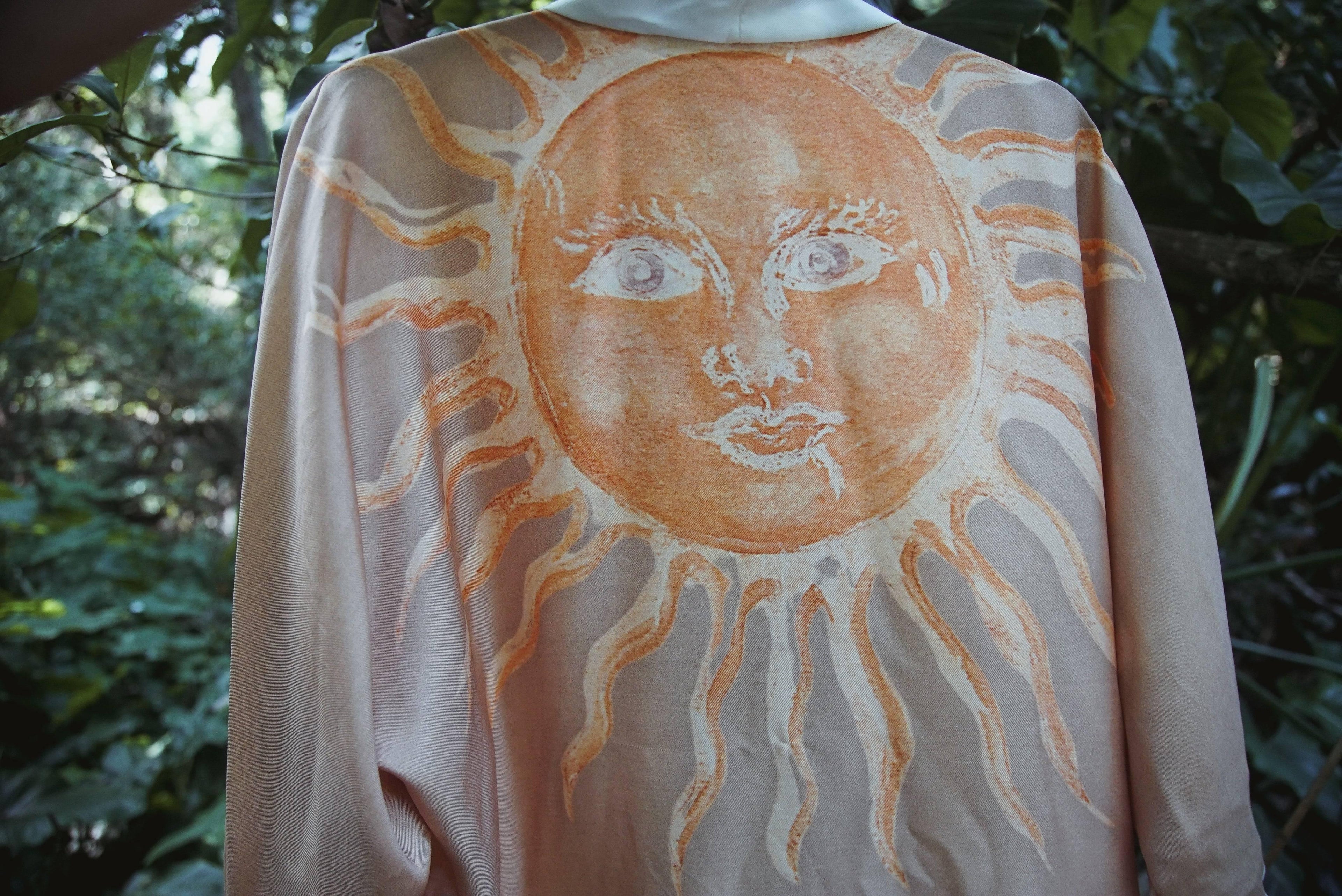 Beige fabric with large artistic sun face design in orange and white, outdoor nature background