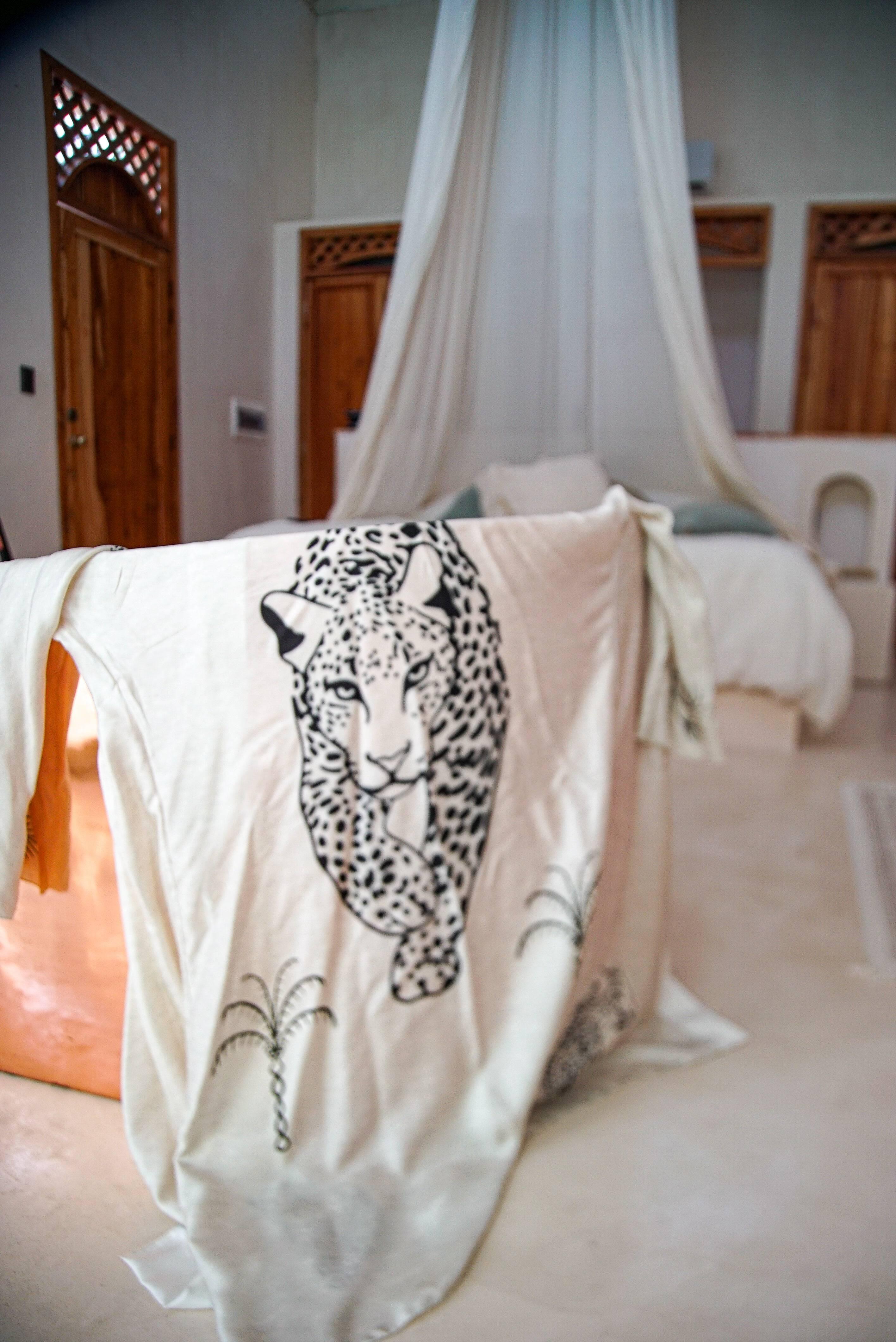 White blanket with black leopard print draped over chair in a cozy bedroom with wooden doors and white canopy bed