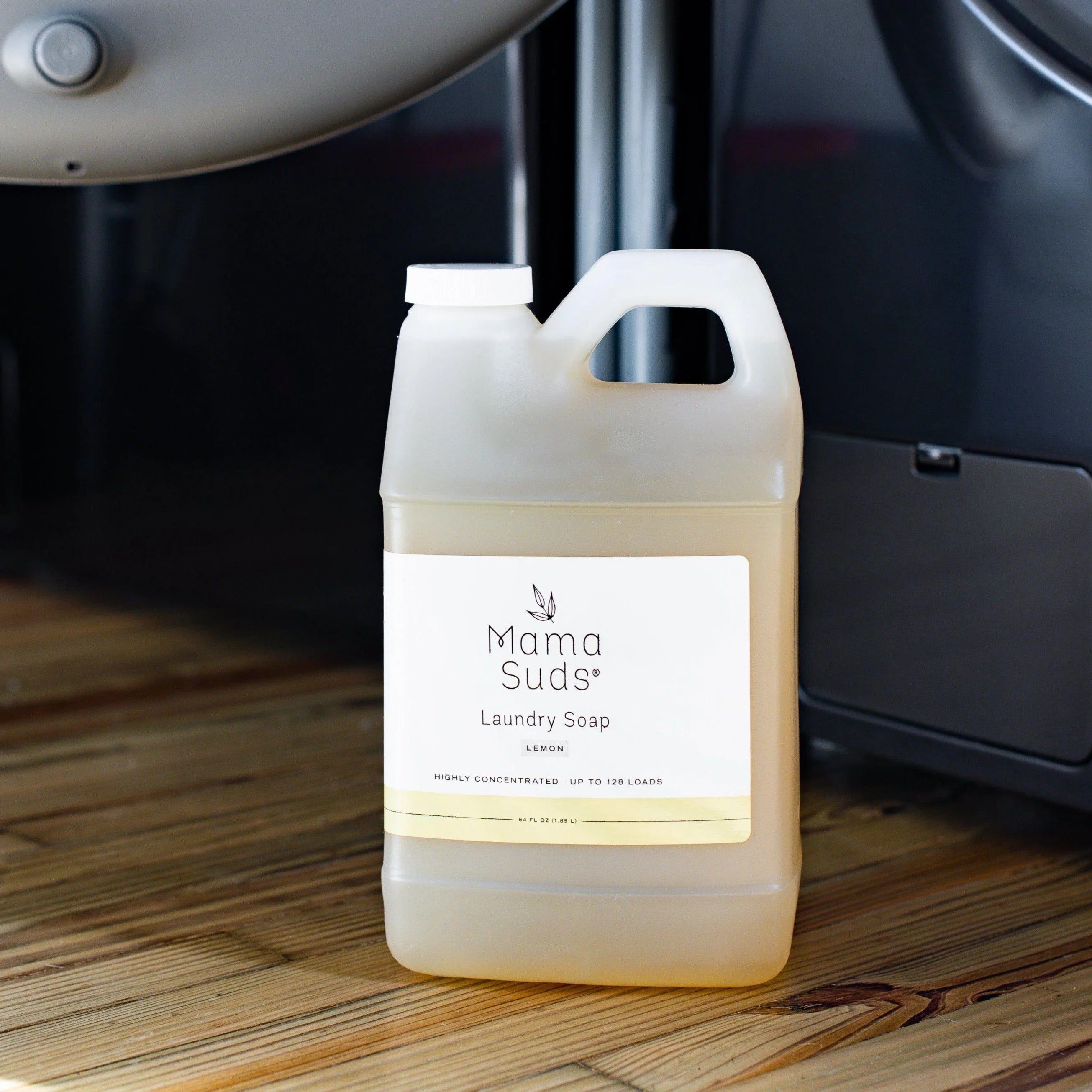 Mama Suds laundry soap lemon scent in jug on wood floor beside washing machine at Quirk Boutique