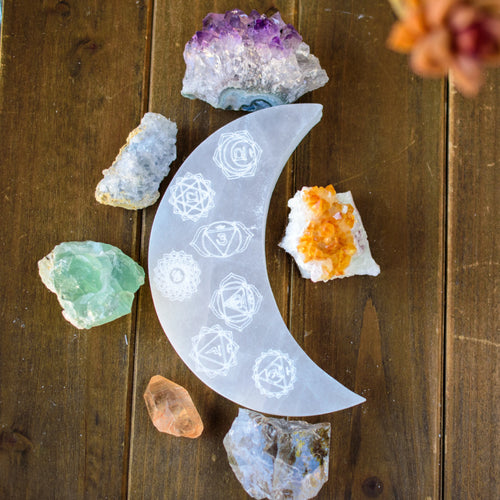 Crescent moon crystal tray with chakra symbols and assorted gemstones on wood table at Qu!rk Boutique