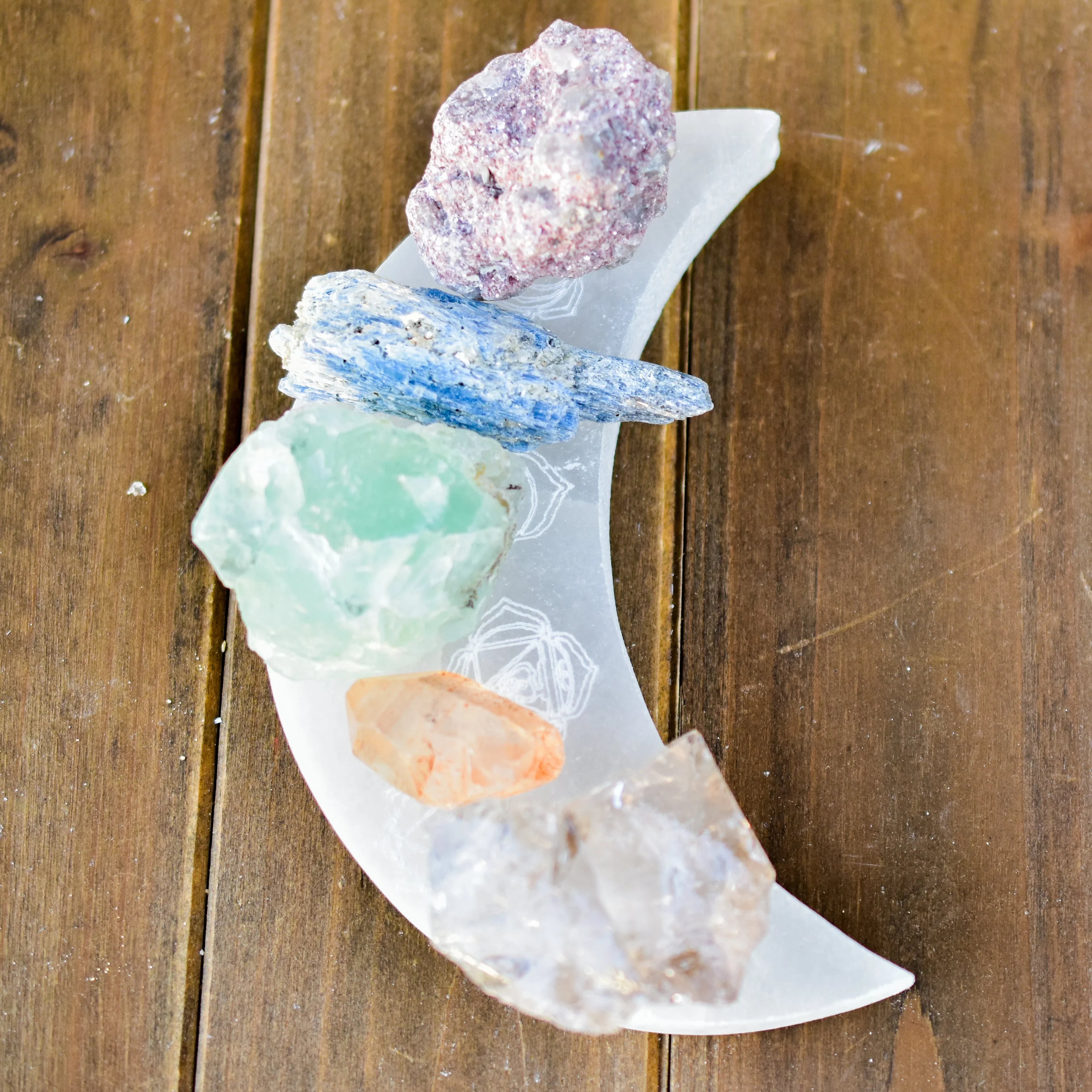 Colorful raw crystals on a moon-shaped dish, displayed on wood at Qu!rk Boutique & Gift Shop