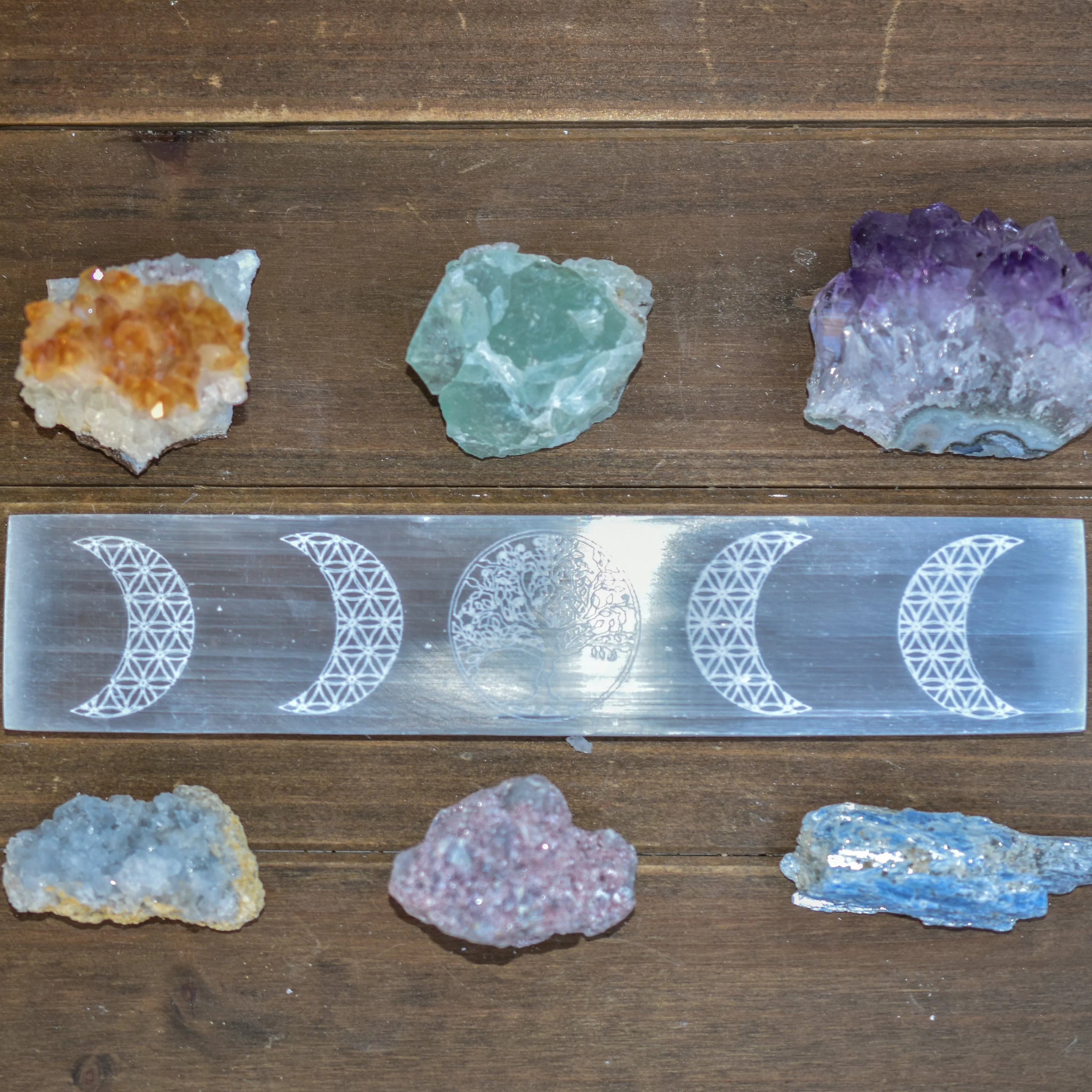 Spiritual crystal collection with orange, green, purple, blue stones and engraved selenite wand on wooden surface
