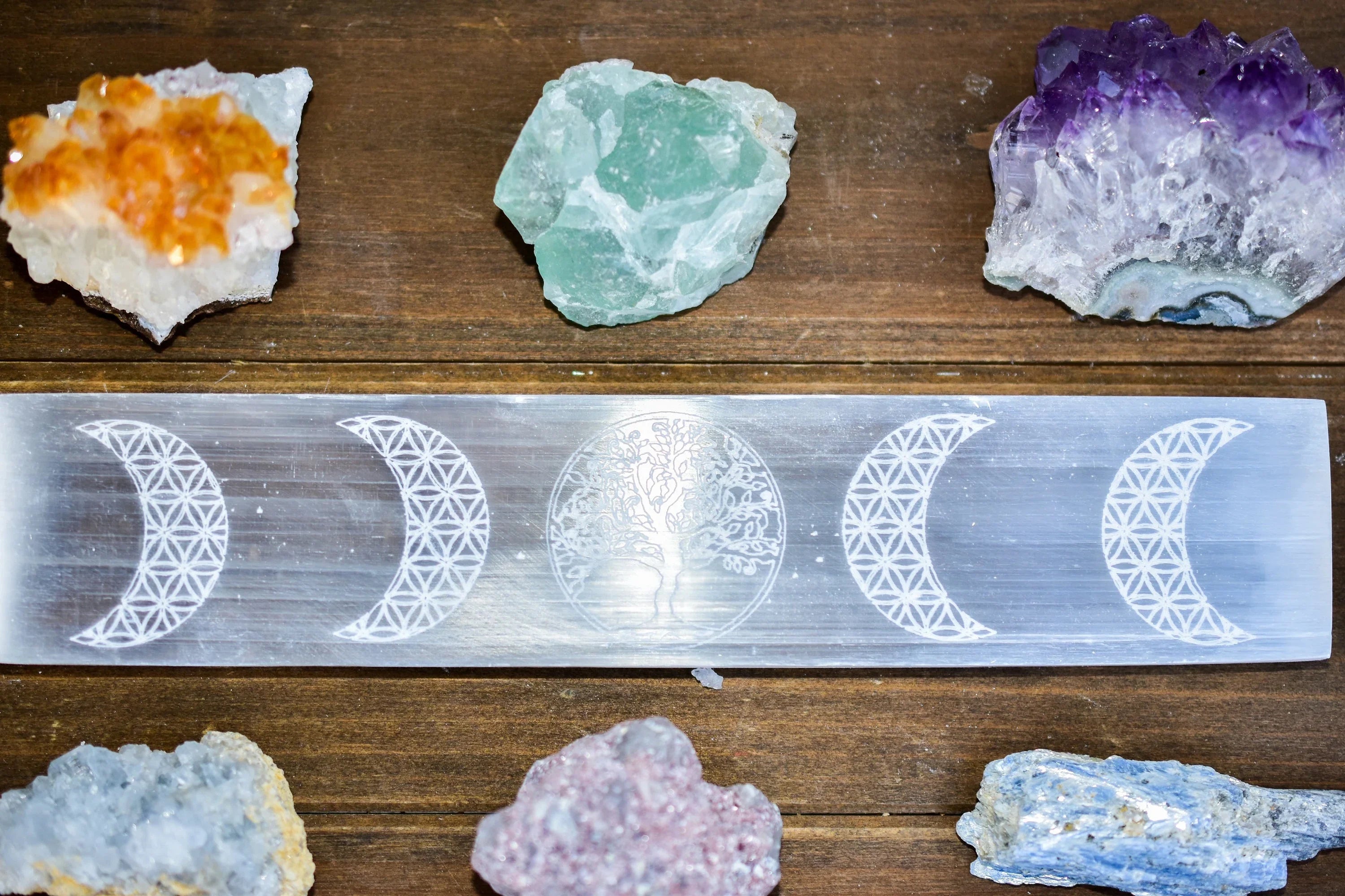 Selenite crystal engraved with tree of life and moon phases, surrounded by colorful healing crystals
