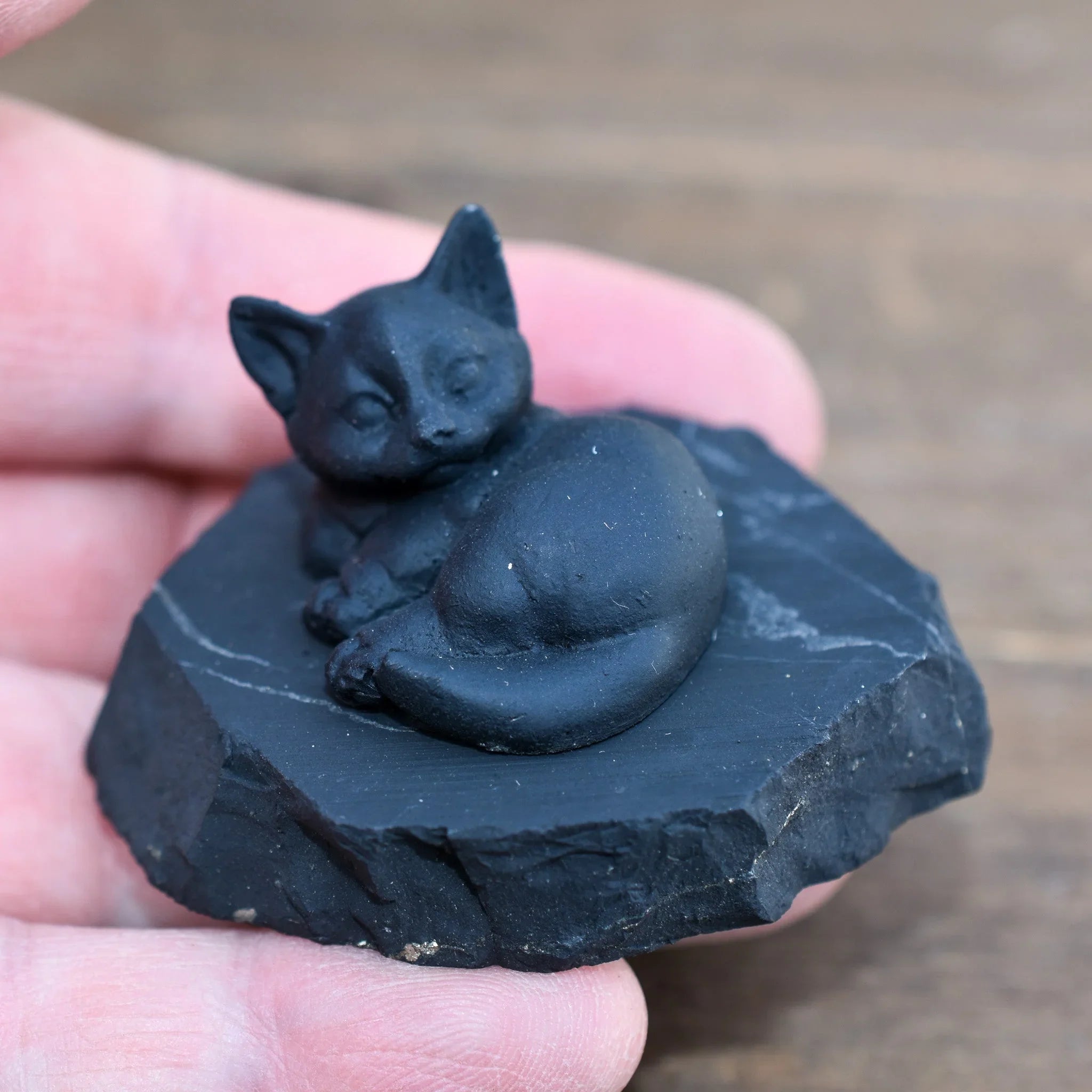 Hand holding a small black fox sculpture on a stone, artisan gift from Qu!rk Boutique