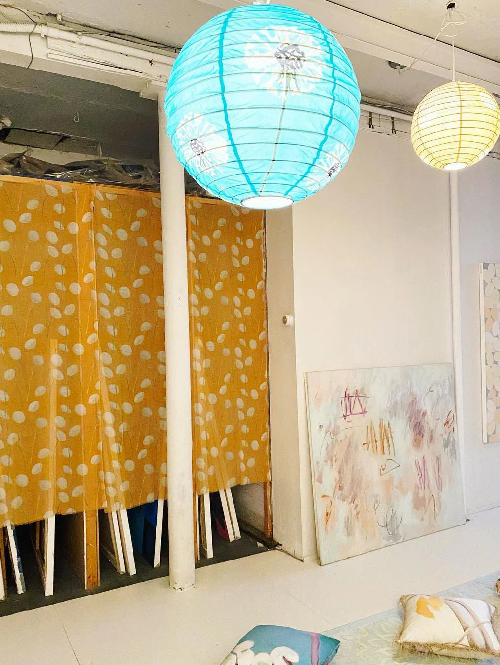 Blue dandelion paper lantern and yellow patterned curtain in cozy art studio with abstract painting