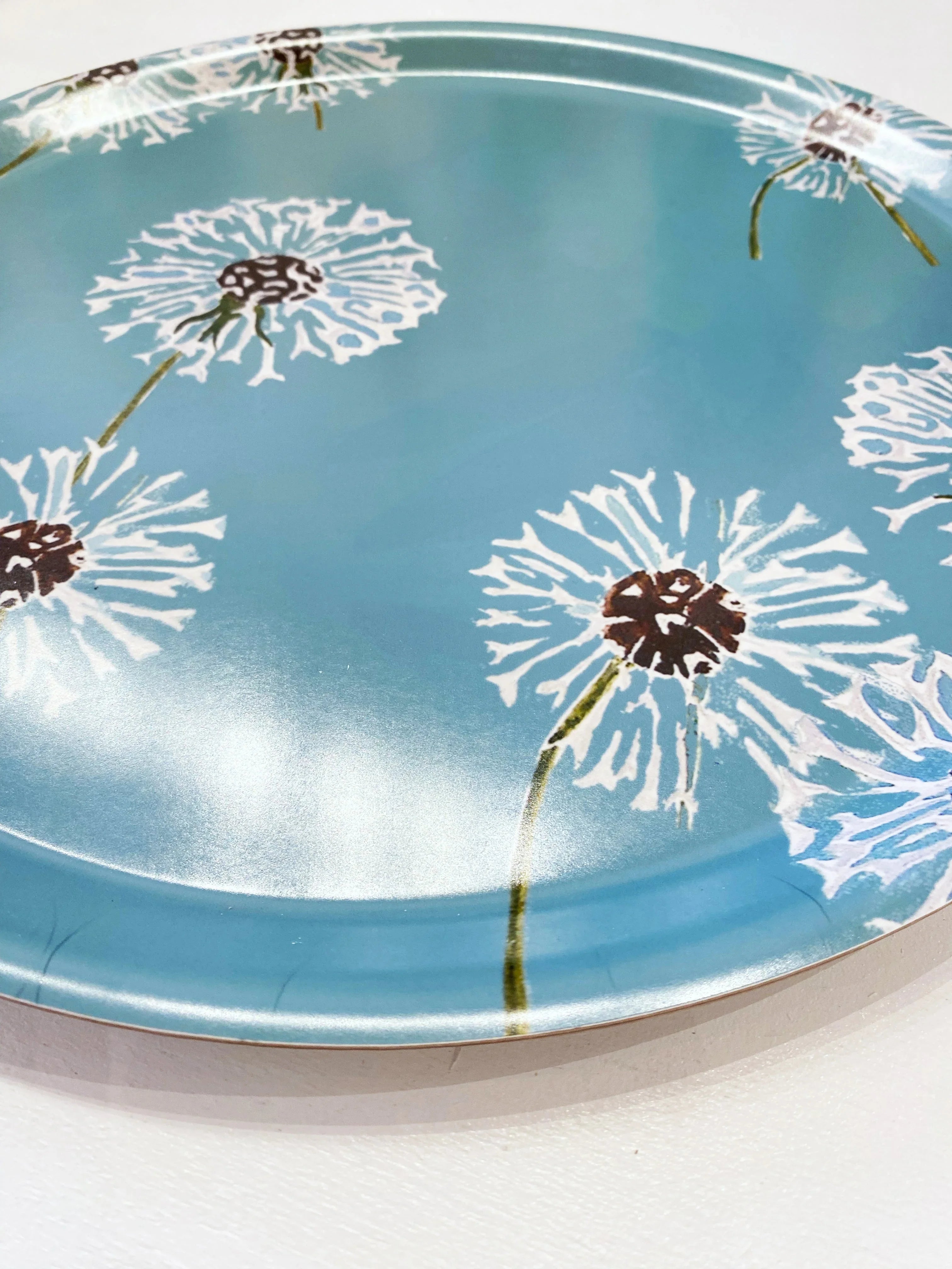 Round blue serving tray with white dandelion flower designs and brown centers