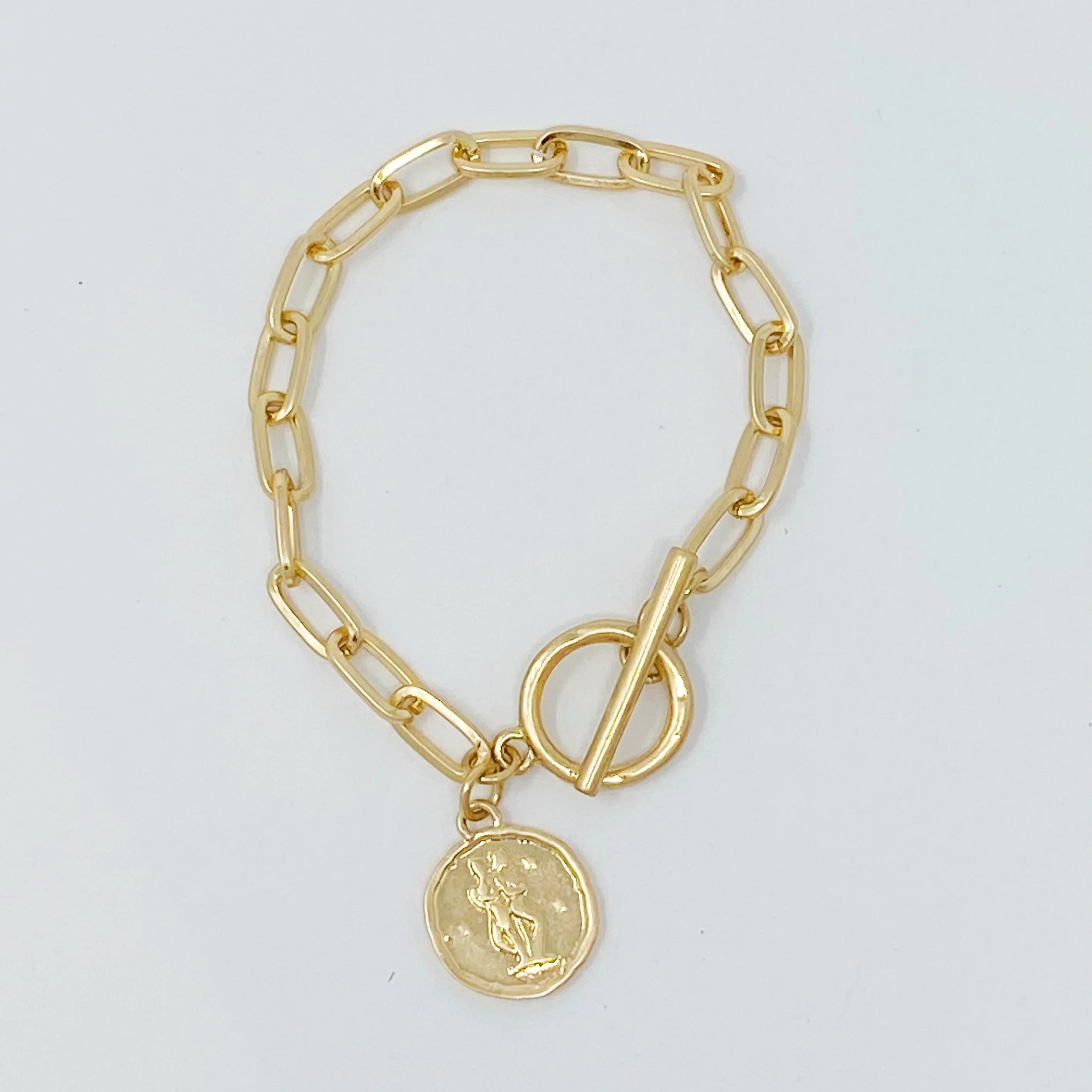 Gold chain link bracelet with round coin charm and toggle clasp on white background