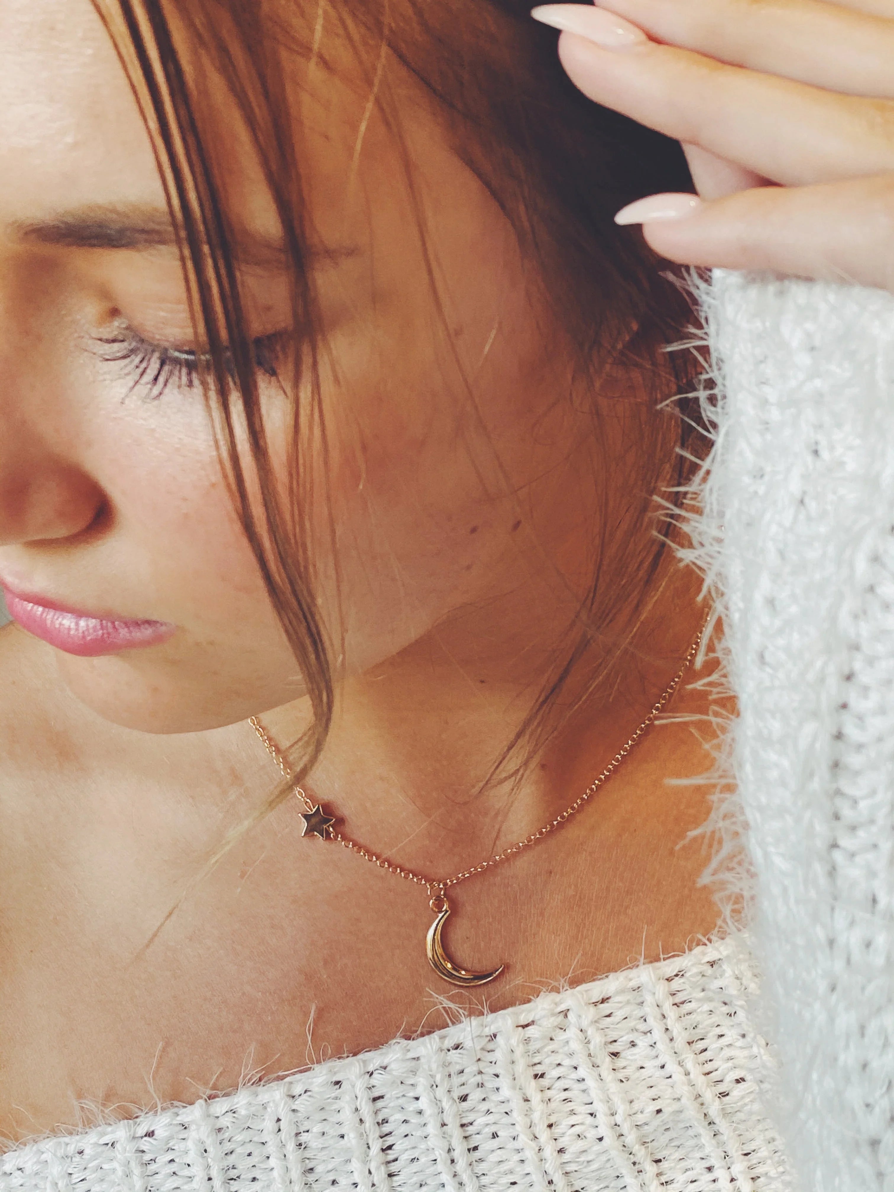 Close-up of woman wearing a gold star and moon pendant necklace with white knitted sweater