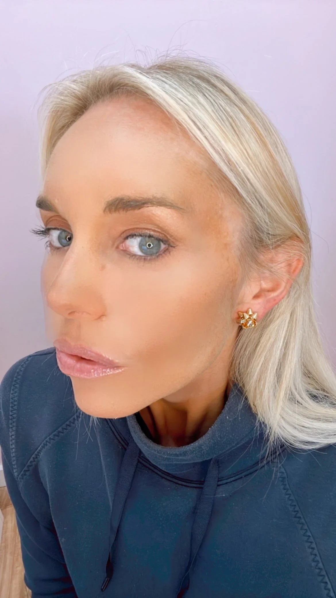 Close-up of woman with blonde hair wearing gold star-shaped stud earrings and navy hoodie