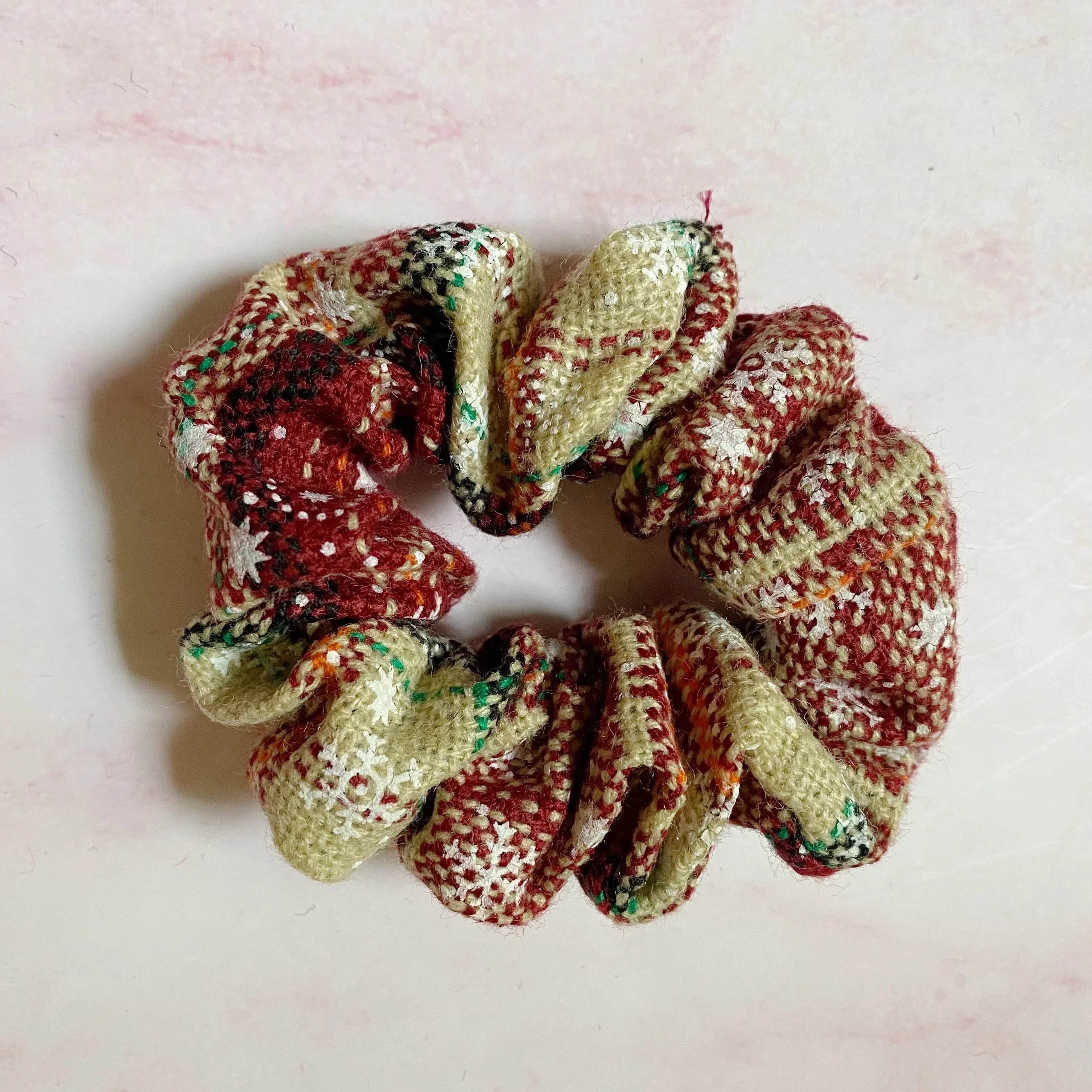 Red and beige plaid fabric scrunchie with winter-themed patterns on light pink background
