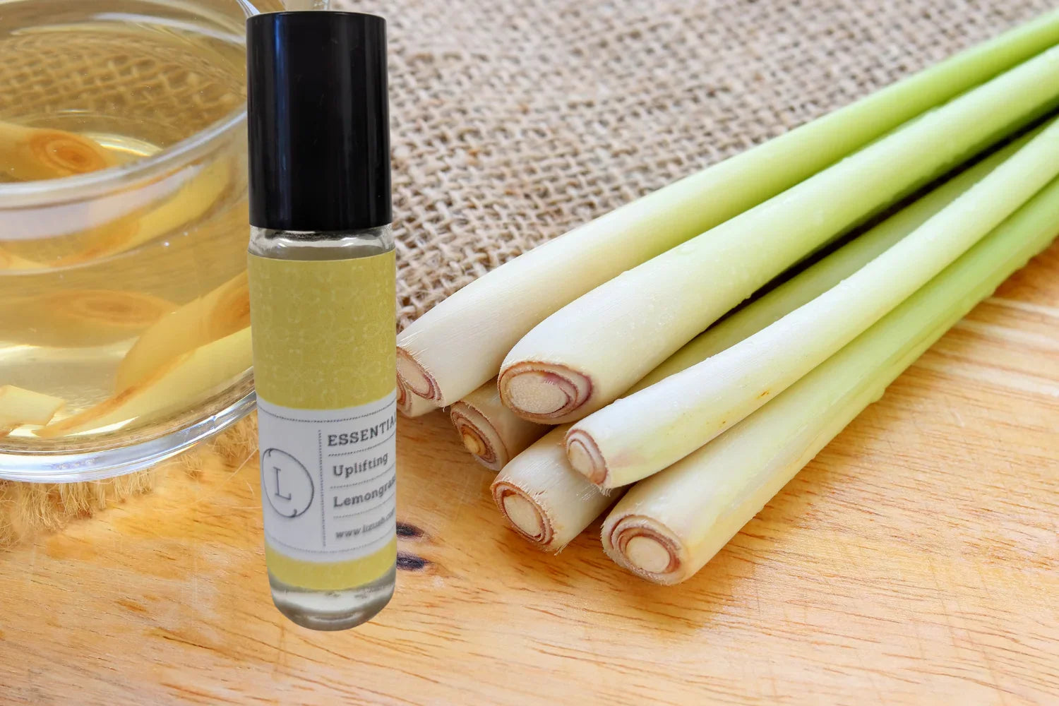 Roll-on lemongrass essential oil bottle beside fresh lemongrass stalks and a cup on wooden surface