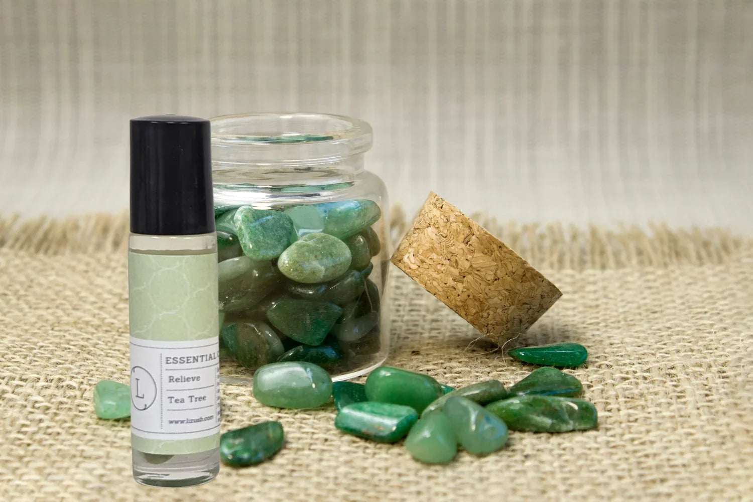 Tea tree essential oil roller bottle and glass jar with green polished healing crystals on burlap
