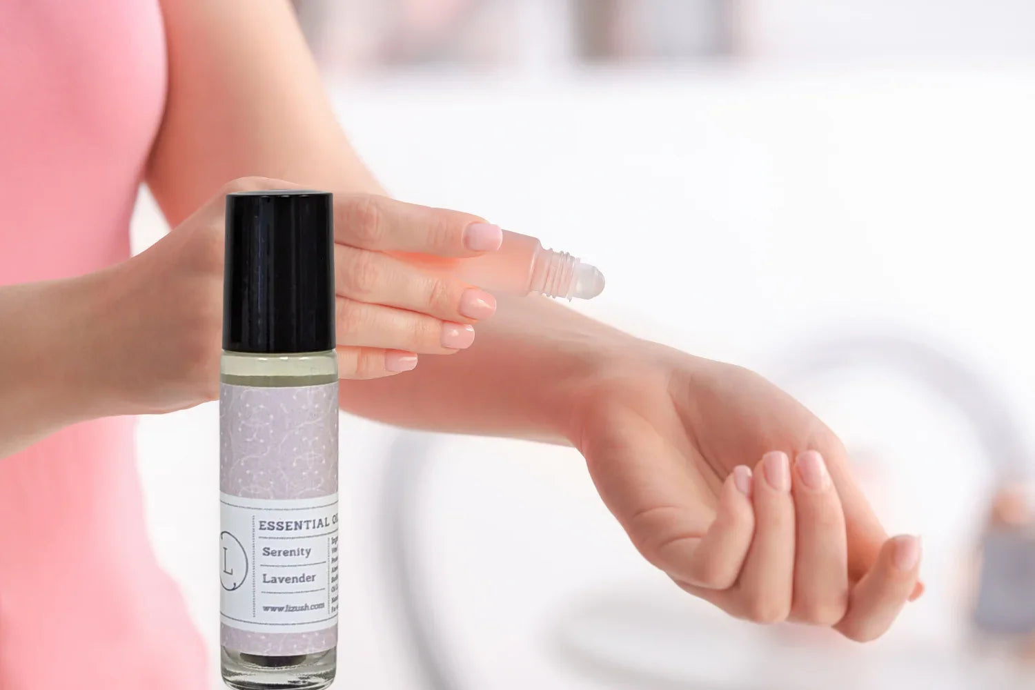 Person applying Serenity Lavender essential oil roller on wrist with pink shirt background