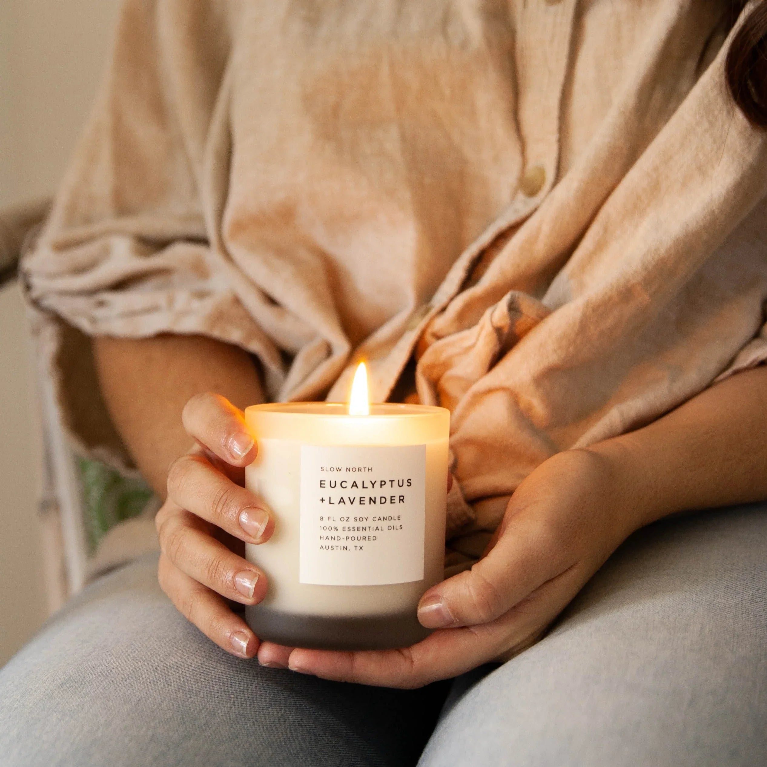 Woman holding a lit Slow North Eucalyptus Lavender soy candle, cozy boutique setting.