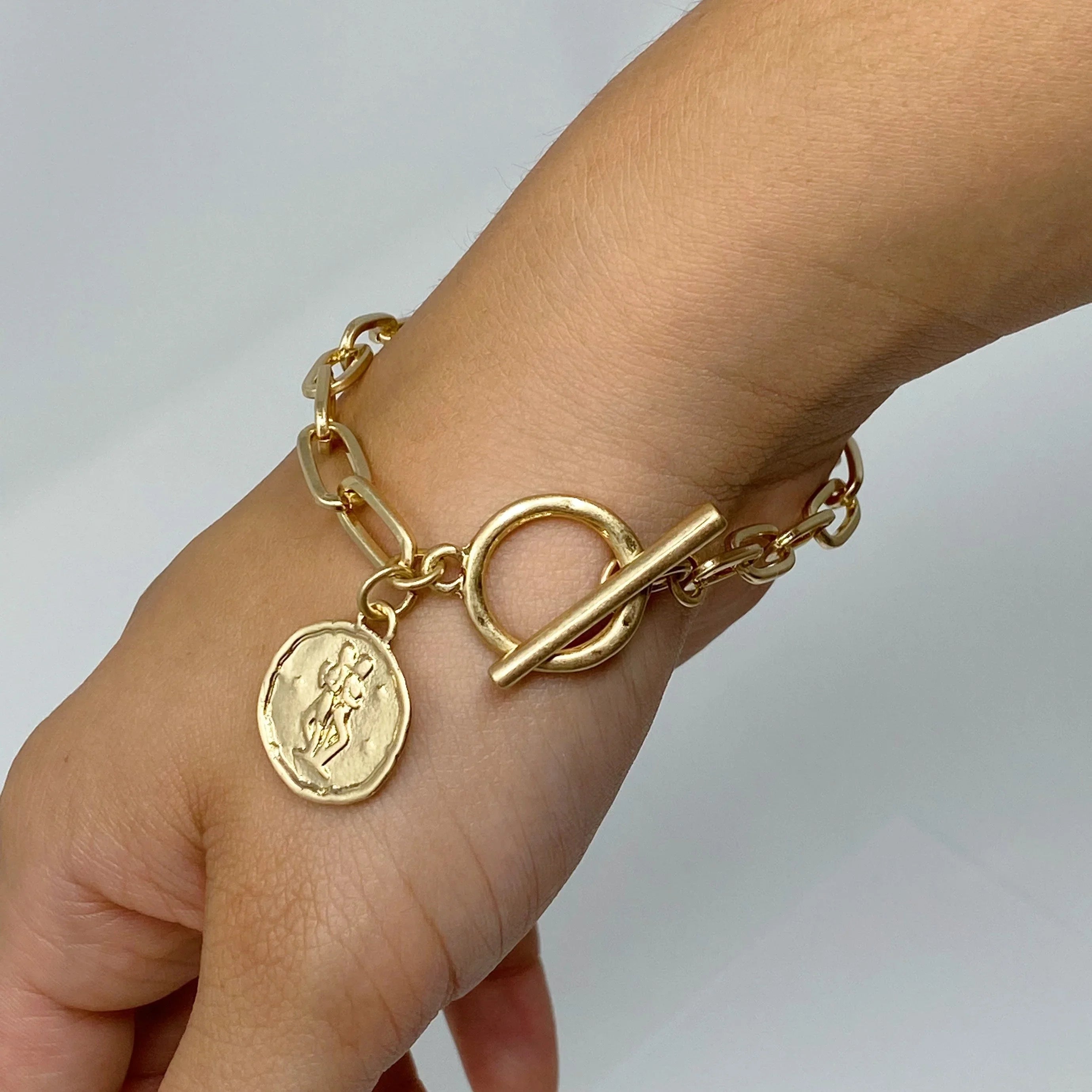 Gold chain link bracelet with round coin charm and toggle clasp on wrist