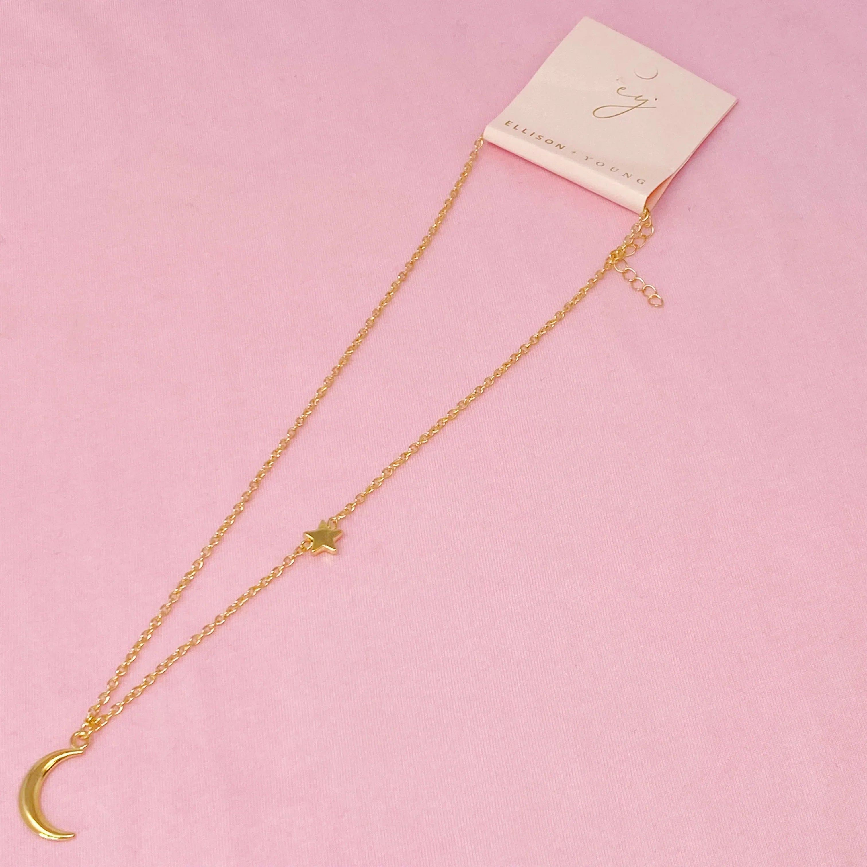 Ellison + Young gold layered necklace with crescent moon and star charms on pink background