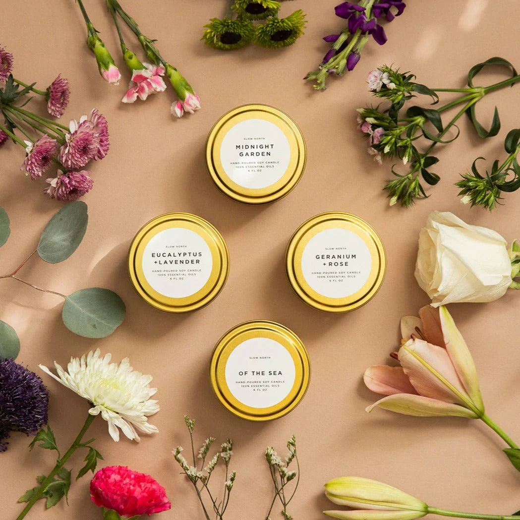 Slow North floral soy candles with gold lids, surrounded by fresh flowers on neutral background