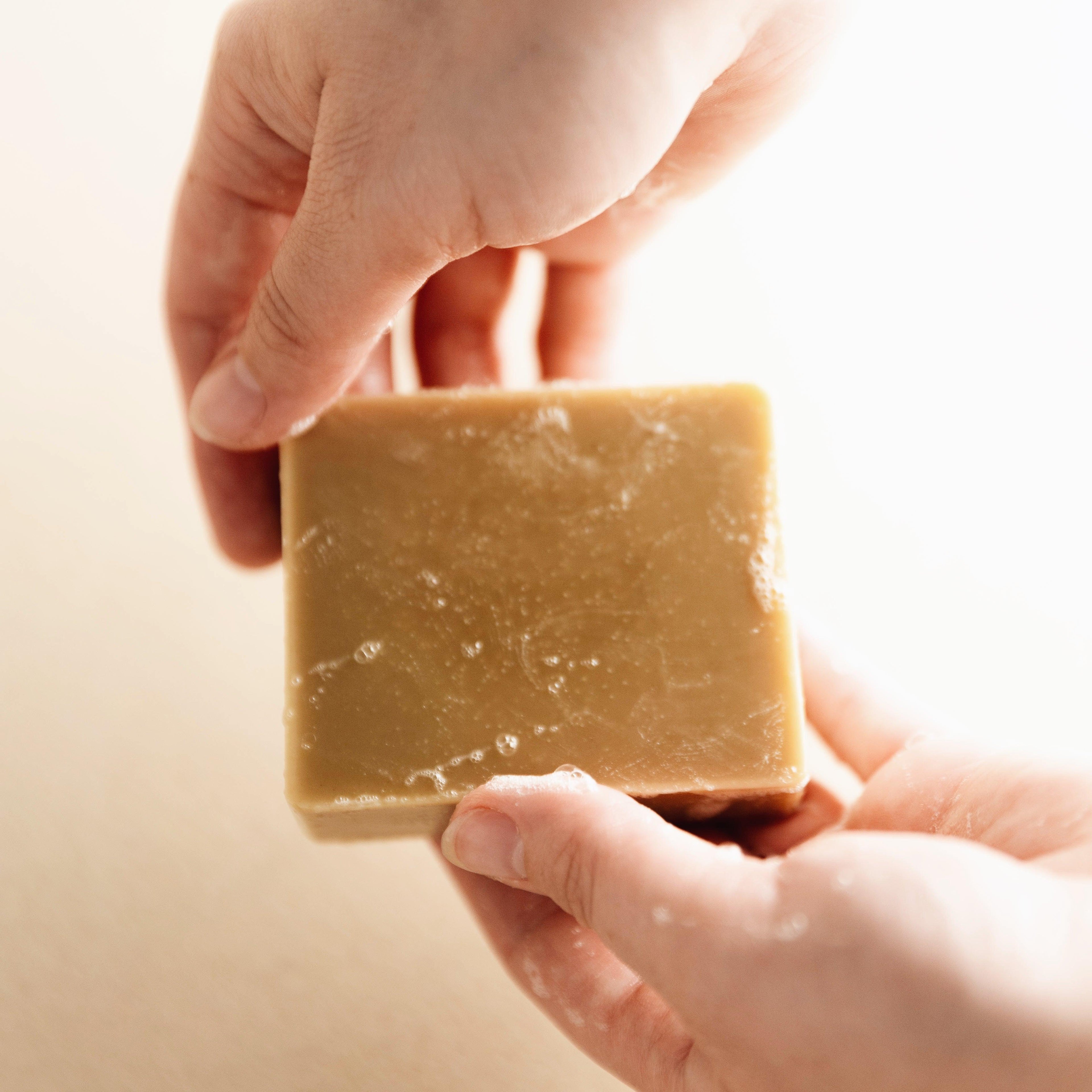 Hands holding a wet rectangular natural bar soap with a beige color and suds