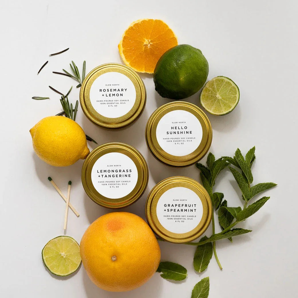 Four gold tins of Slow North hand-poured soy candles with citrus fruits and herbs on white background
