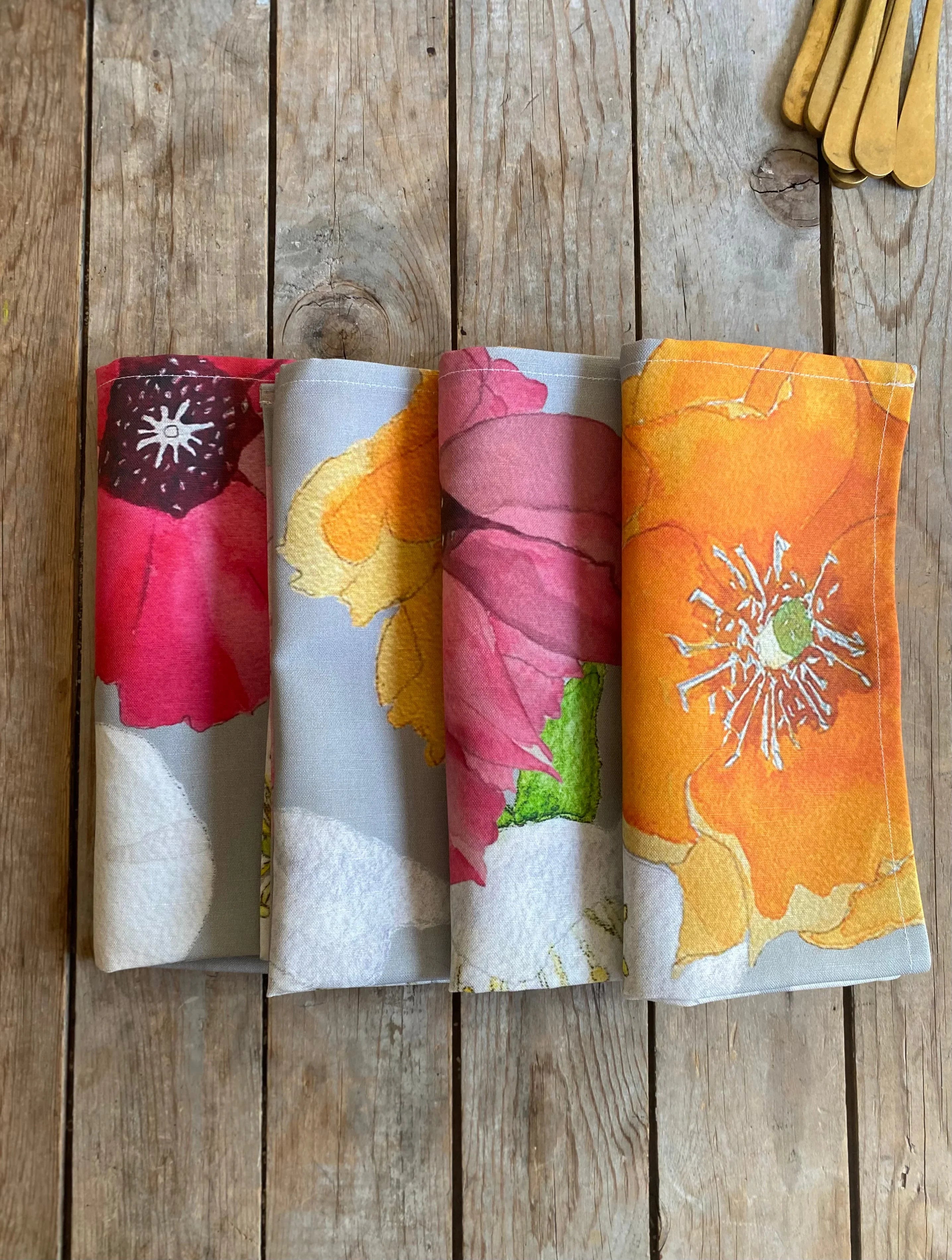 Four folded floral print cloth napkins with bright red, yellow, pink, and orange flowers on wooden table
