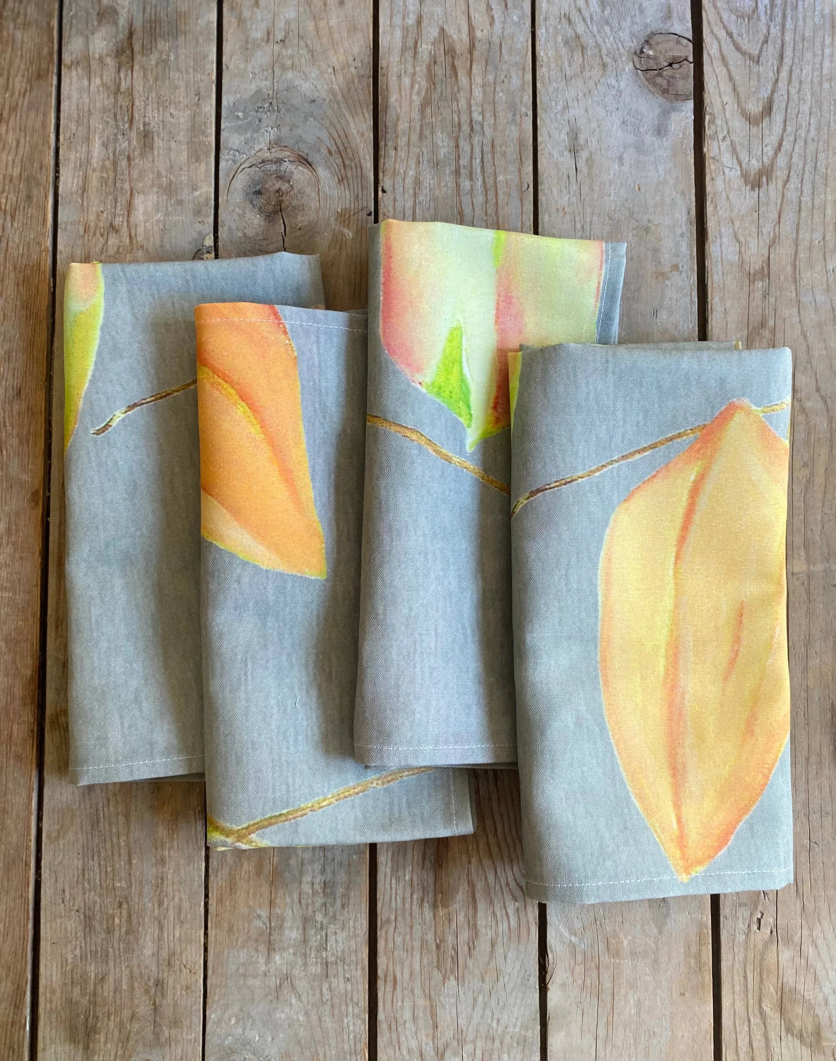 Set of four folded fabric napkins with orange-yellow leaf prints on a wooden surface
