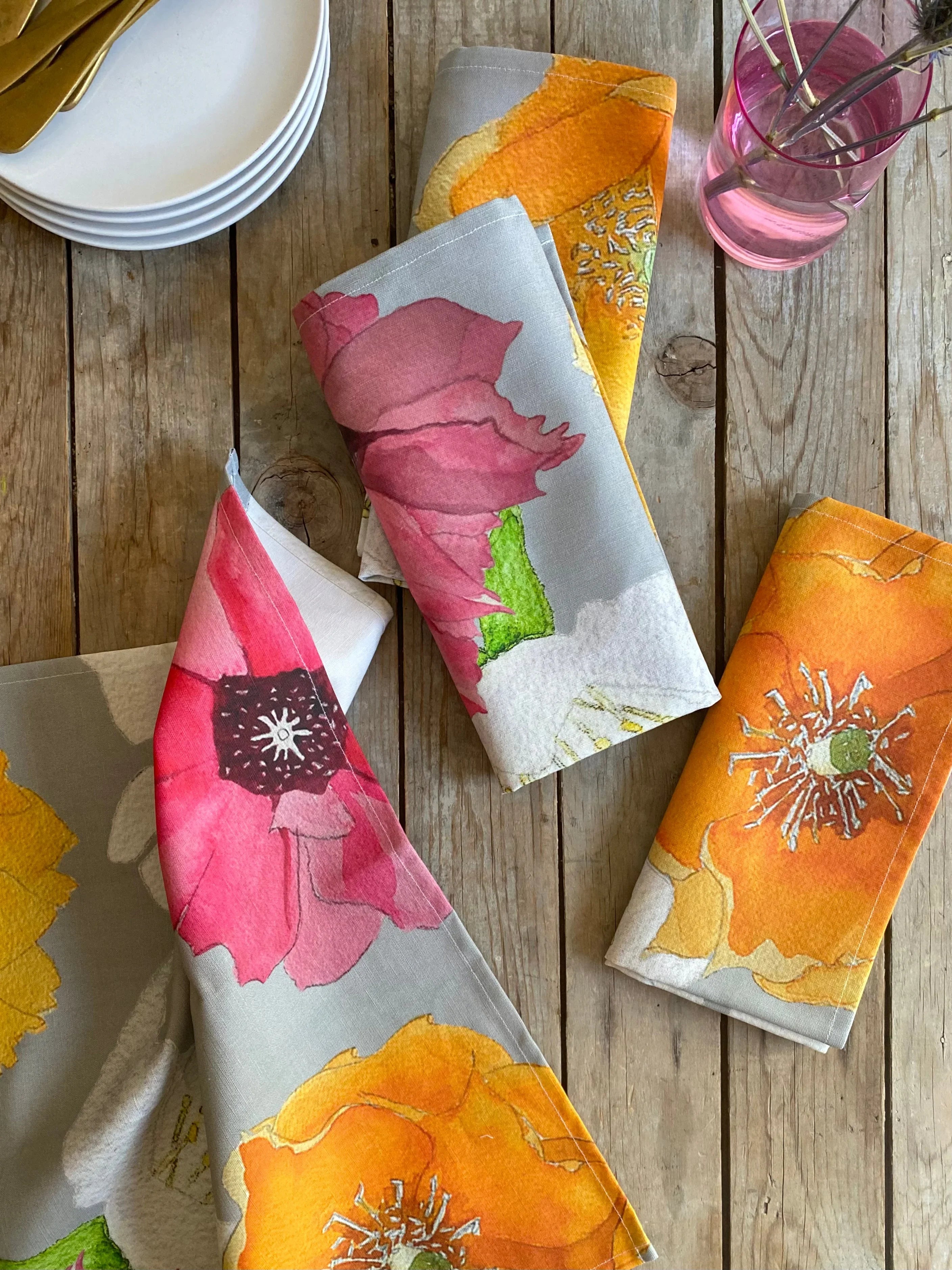 Floral patterned linen napkins in orange, pink, and white on rustic wooden table with white plates and pink glass vase