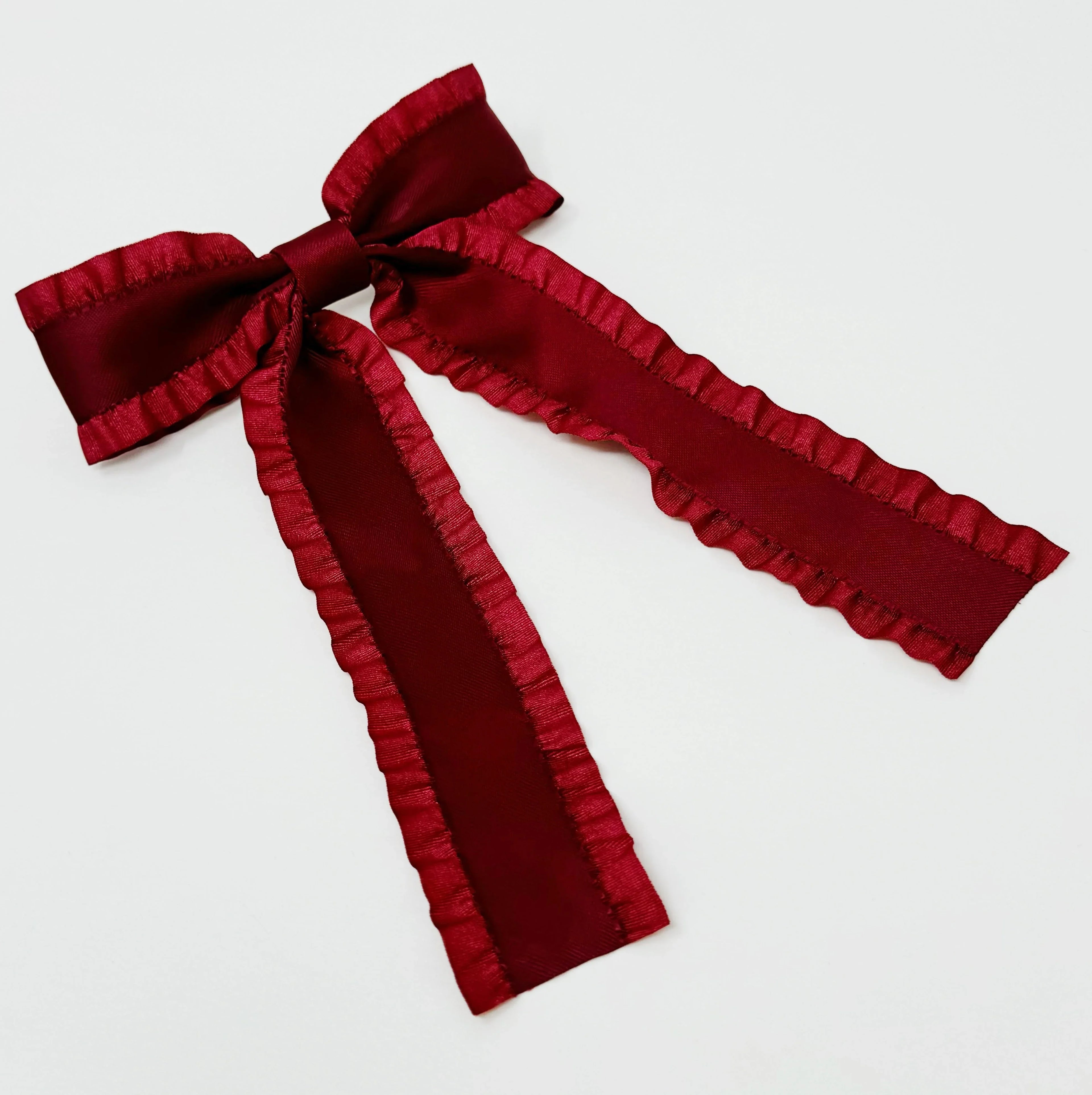 Deep red satin bow with ruffled edges on white background, decorative ribbon accessory