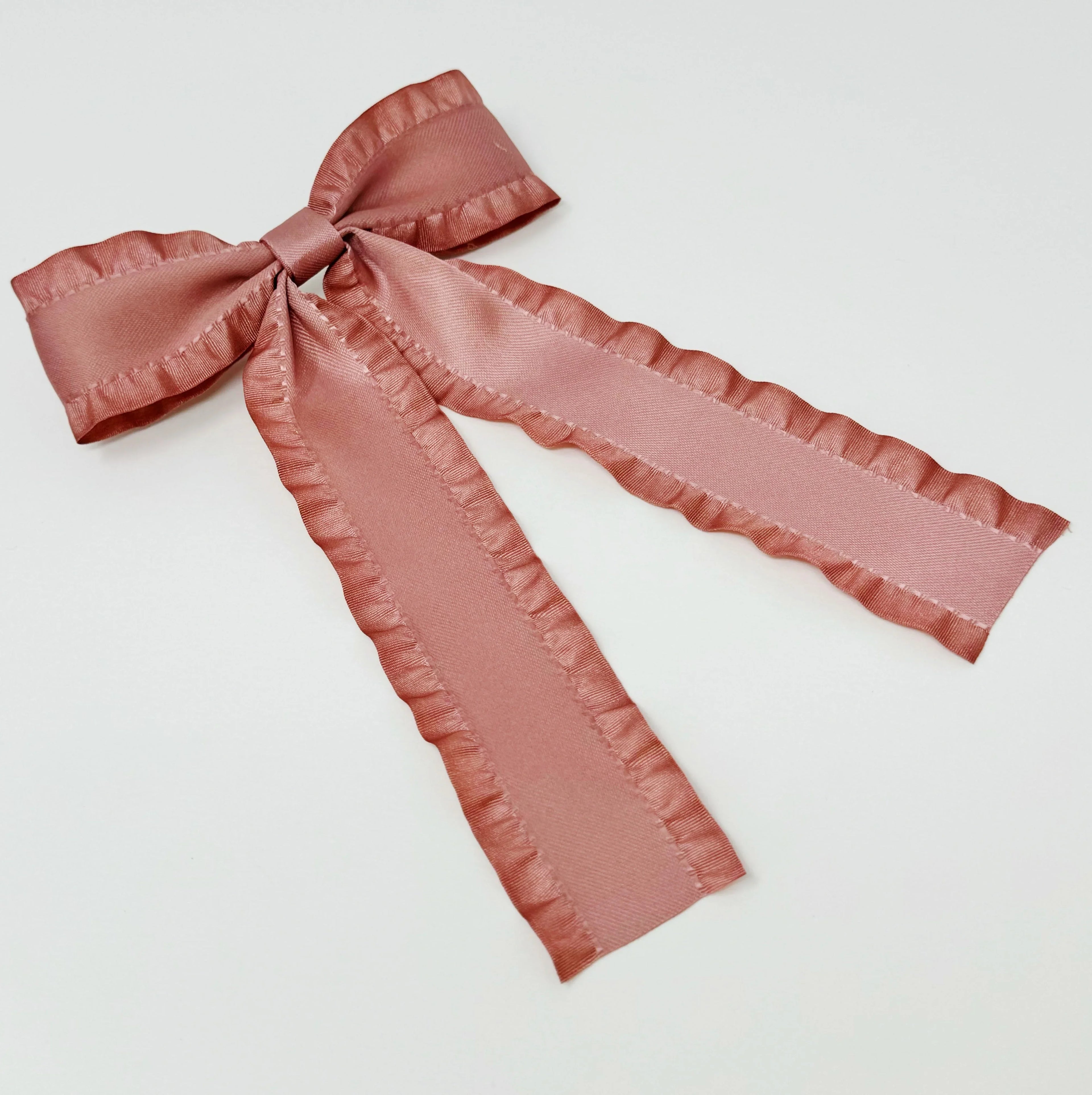 Dusty pink satin ribbon bow with ruffled edges on white background