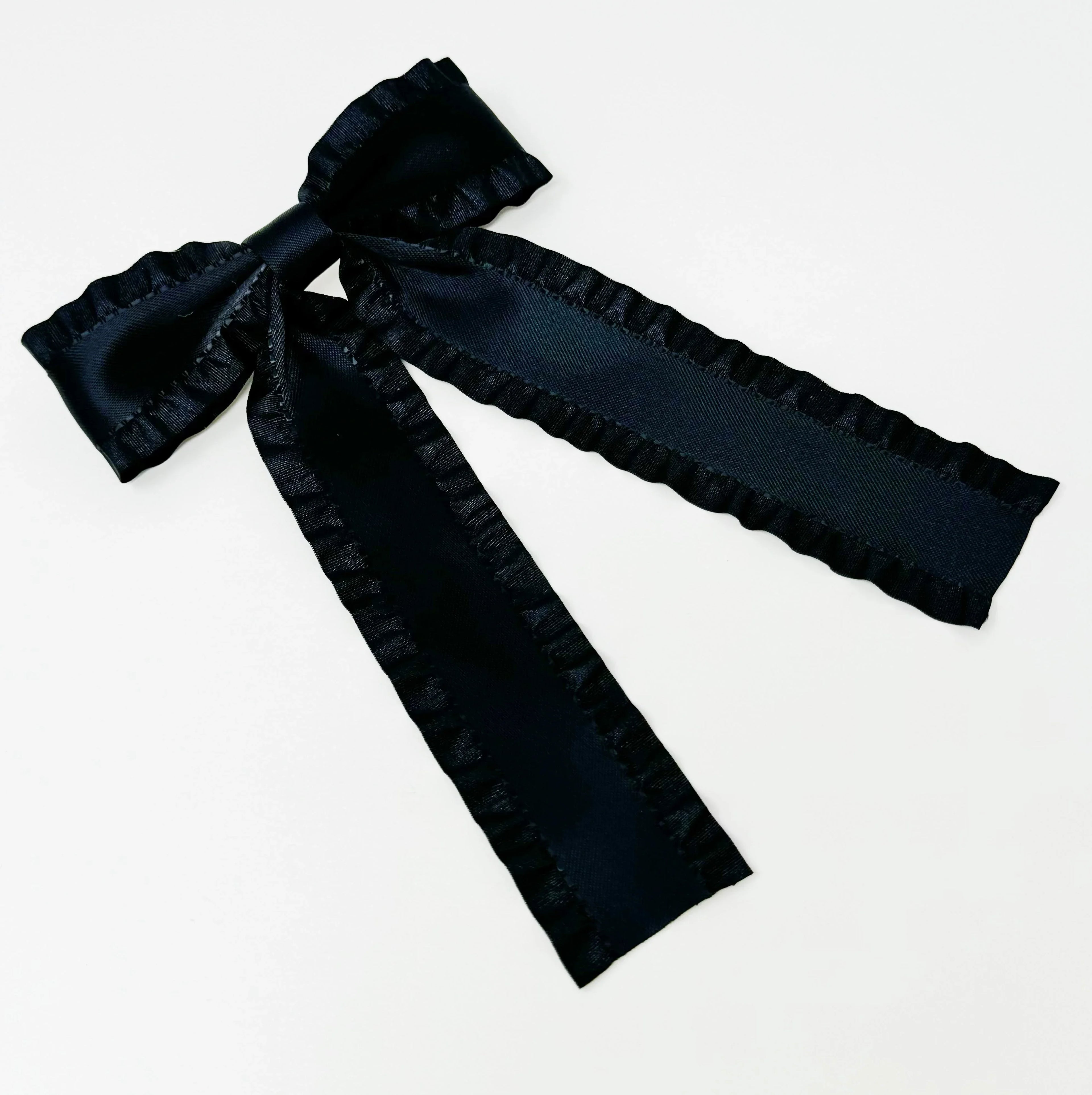 Black satin bow with ruffled edges on a white background, decorative hair accessory