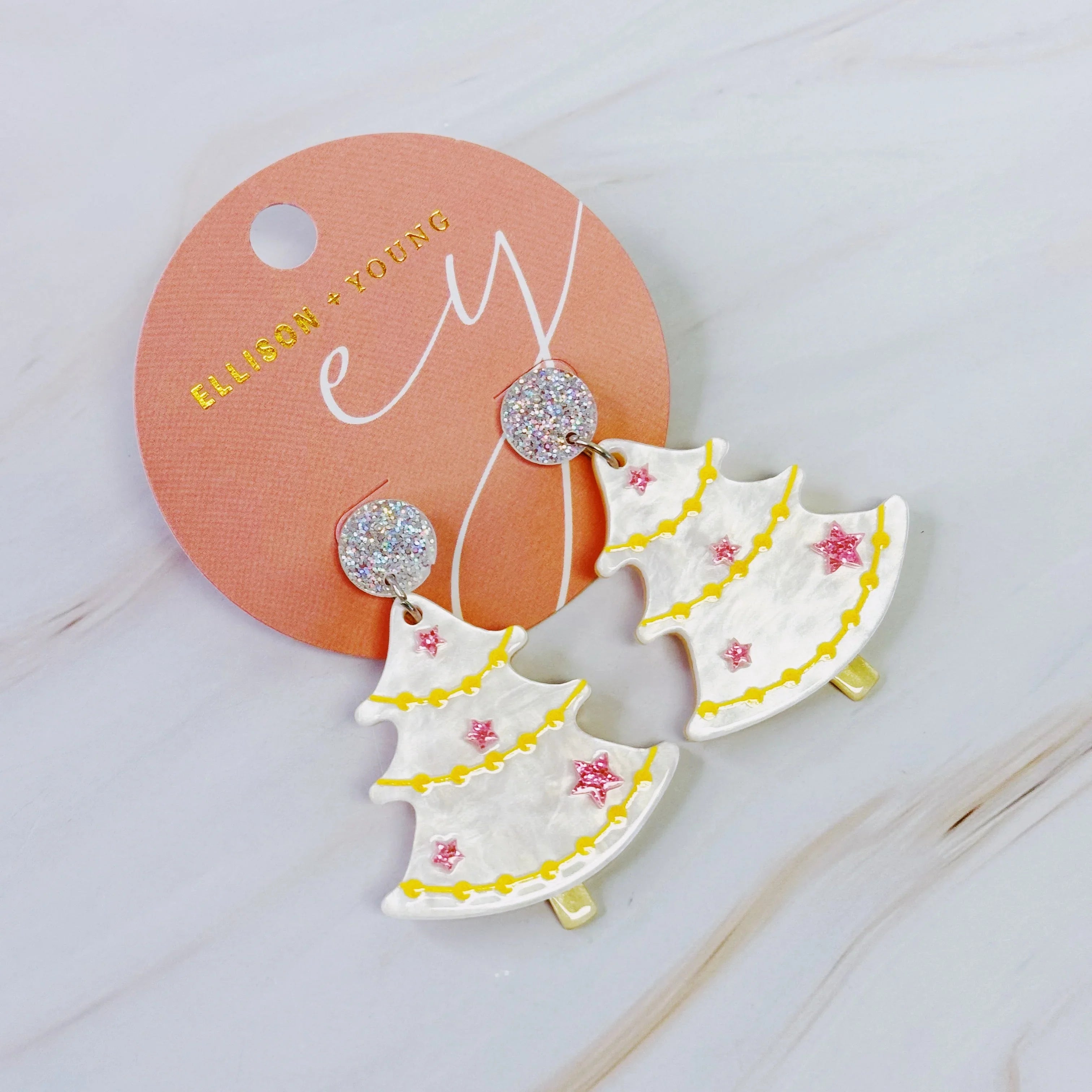 Ellison + Young festive Christmas tree earrings with glittery pink stars and yellow garlands on a peach card
