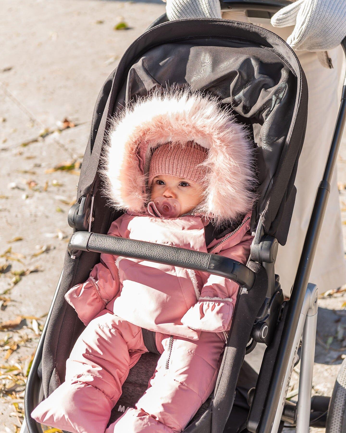 Baby in pink winter snowsuit with faux fur hood in stroller, outdoor daytime, Qu!rk Boutique