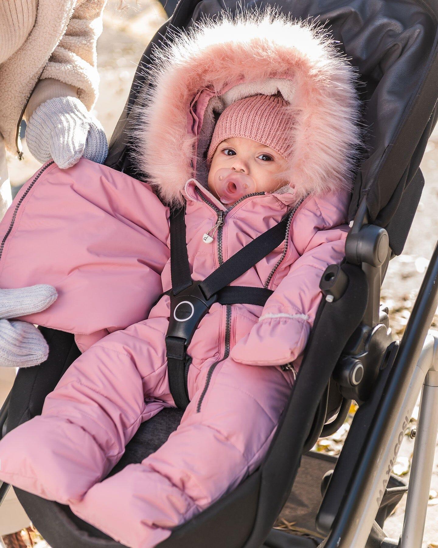 Baby in pink snowsuit with faux fur hood and knit hat, bundled in stroller outdoors, Qu!rk Boutique