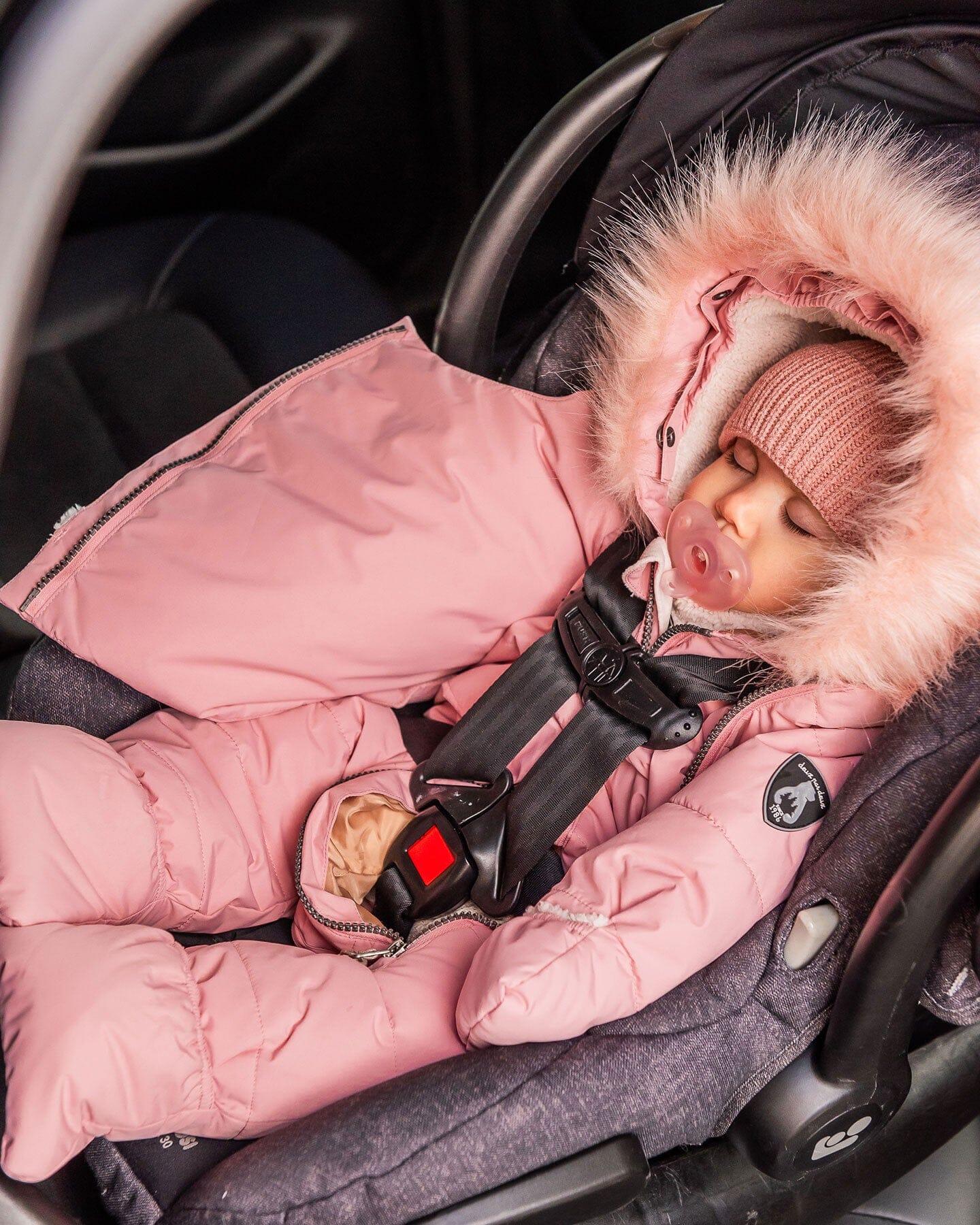Sleeping baby in pink fur-lined snowsuit and knit hat, secured in a car seat