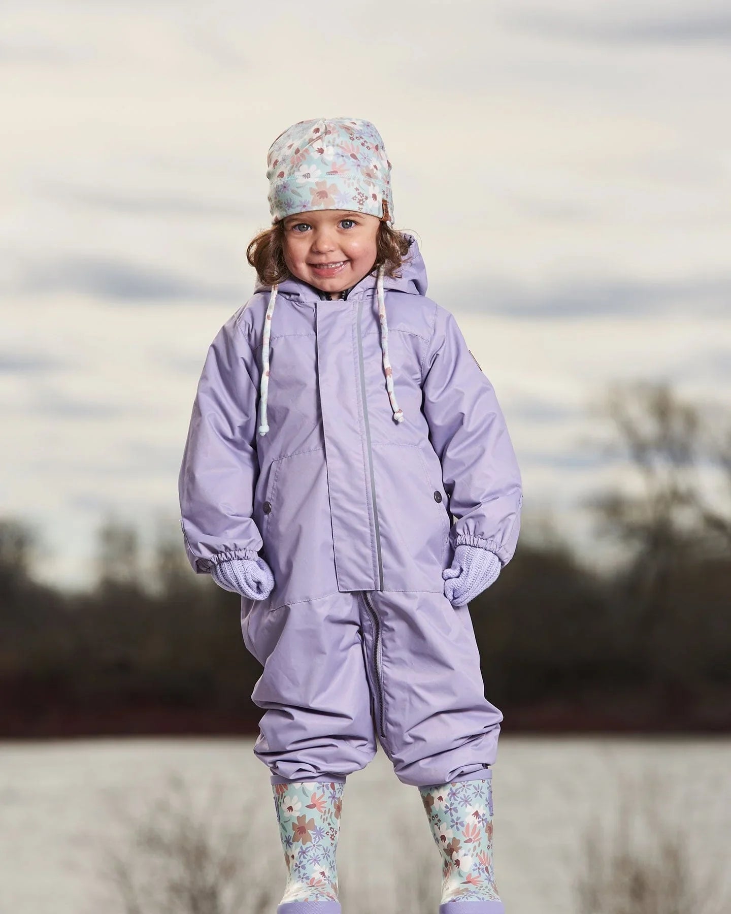Child in pastel purple snowsuit, floral boots and hat, outdoors in winter, Qu!rk Boutique