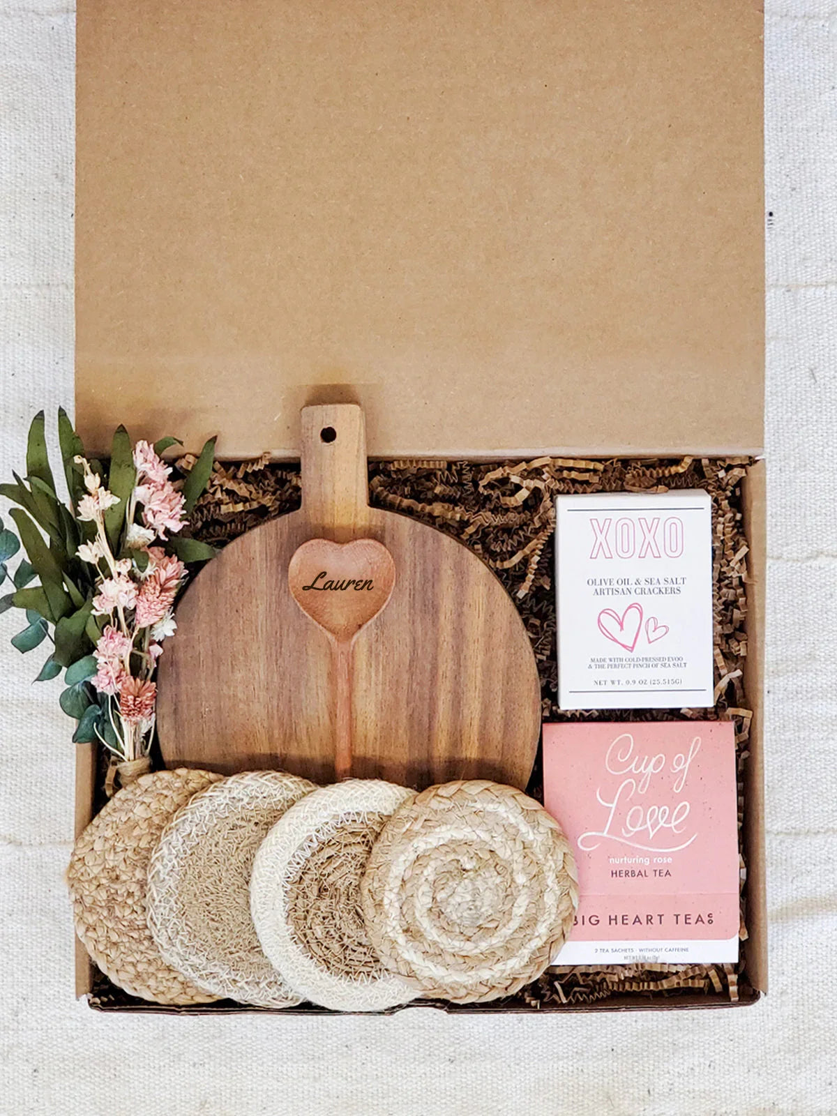 Personalized wooden heart cutting board with Lauren engraving and gift box including herbal tea, crackers, coasters, and flowers
