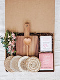 Gift box with wooden cutting board, heart-shaped wooden spoon, artisan crackers, herbal tea, dried flowers, and woven coasters