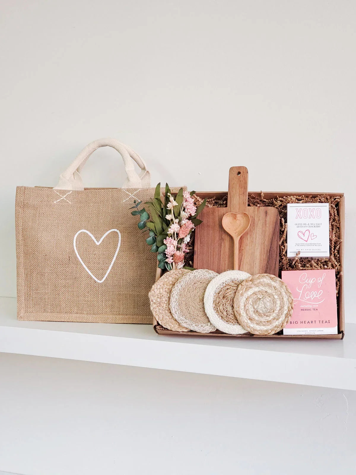 Gift box with wooden heart-shaped spoon, cutting board, coasters, herbal tea, artisanal chocolates, dried flowers, and burlap tote bag