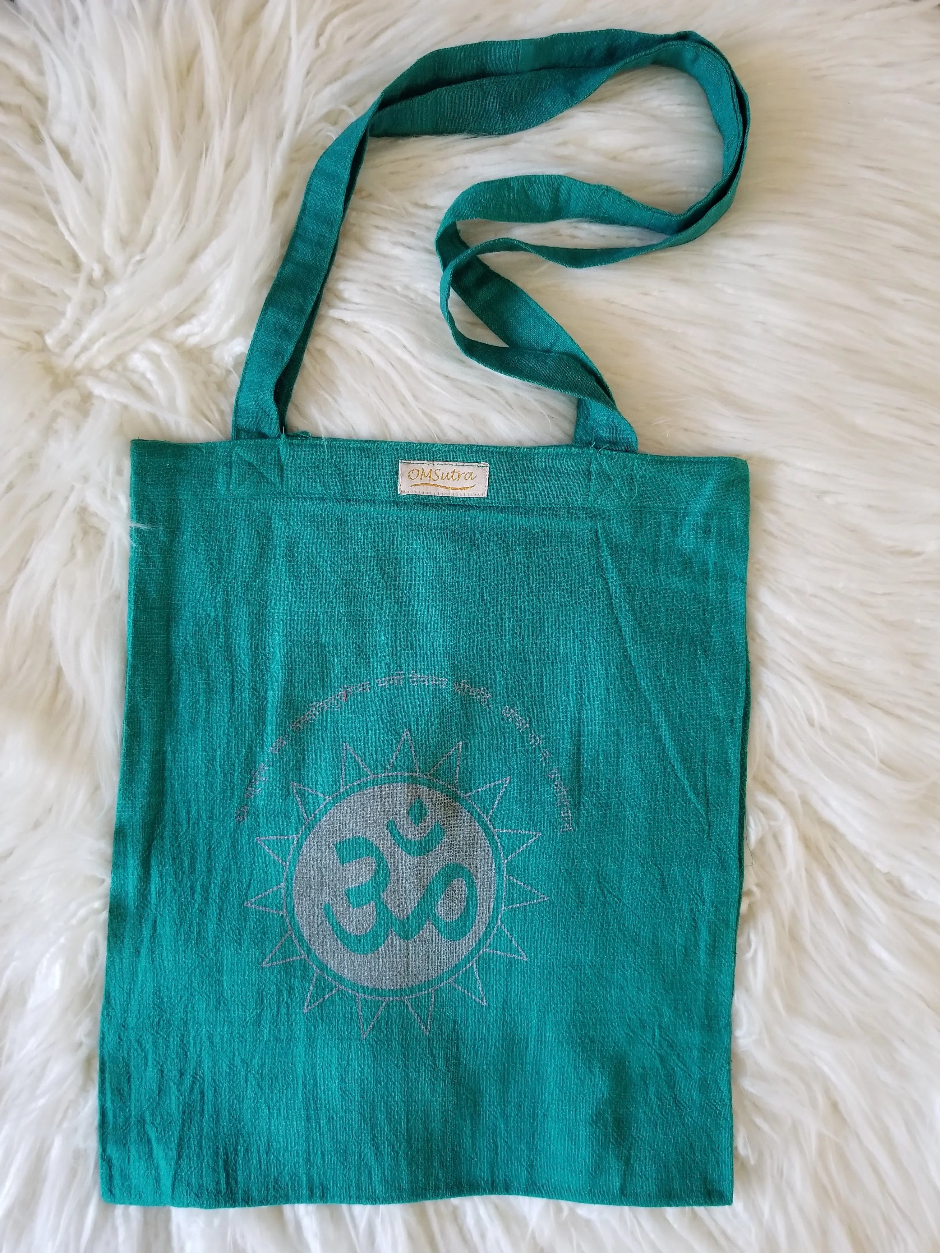 Green cotton tote bag with Om symbol and Sanskrit text, laid on white fur background