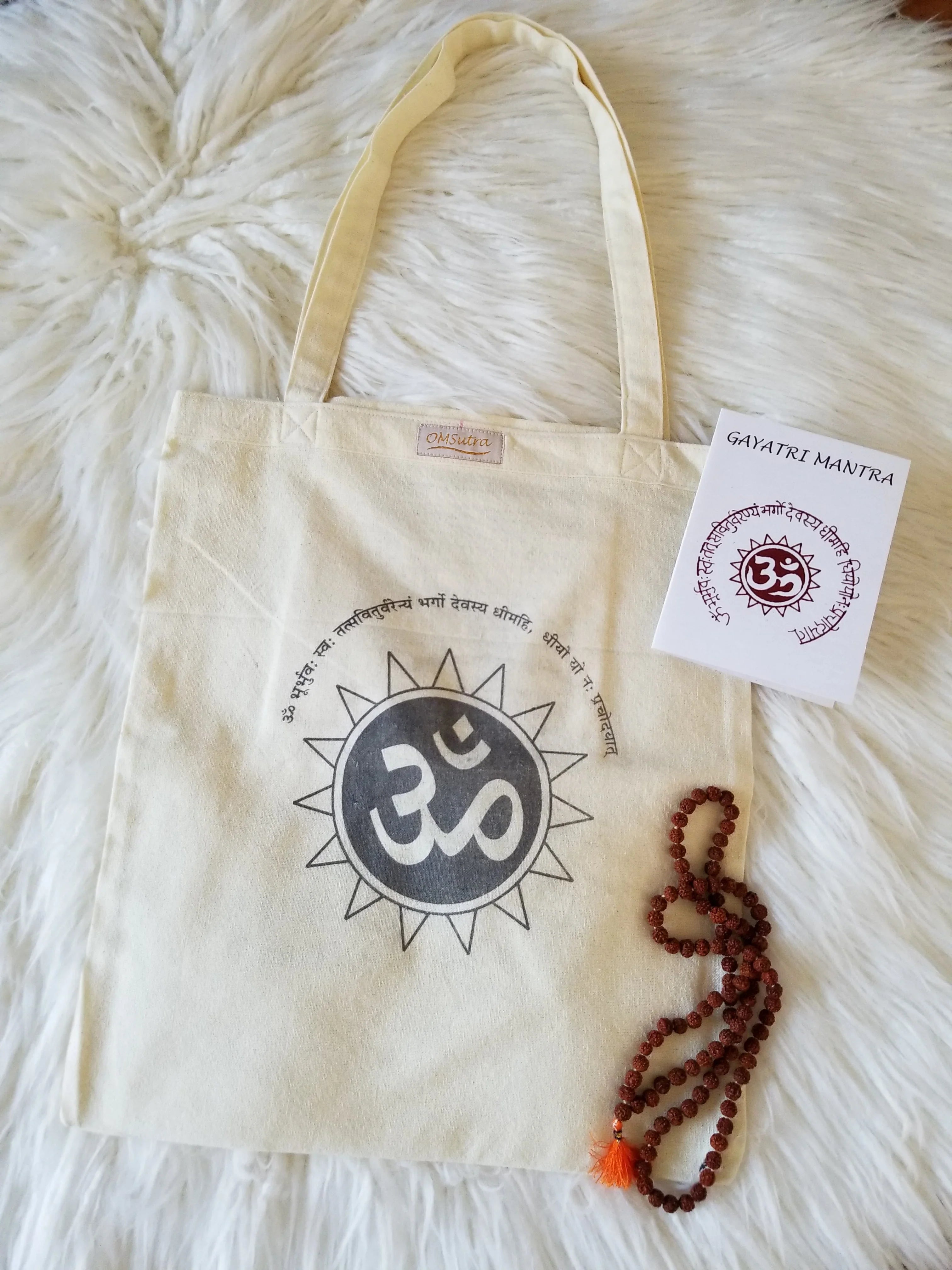 Natural colored tote bag with Om symbol and Gayatri Mantra print, prayer beads, and mantra card on white fur