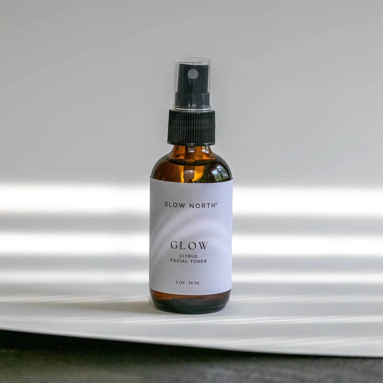 Amber glass bottle of Slow North Glow Citrus Facial Toner with black spray cap on white surface