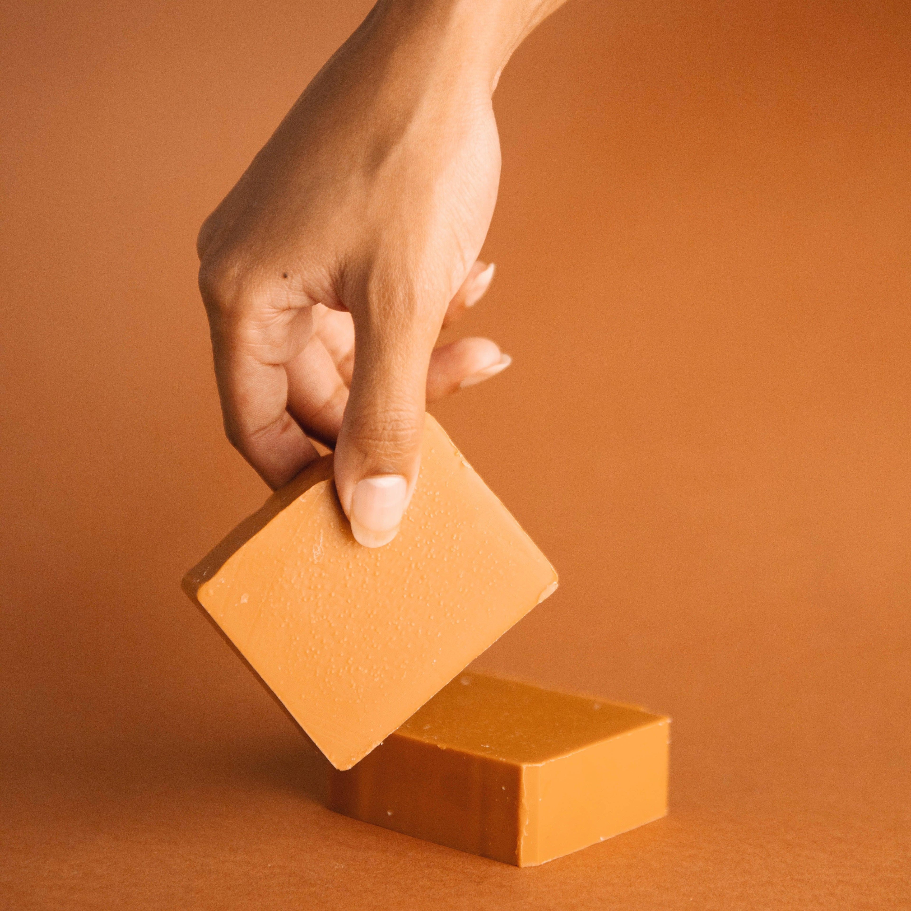 Hand holding an orange grapefruit spearmint scented natural bar soap against a matching orange background