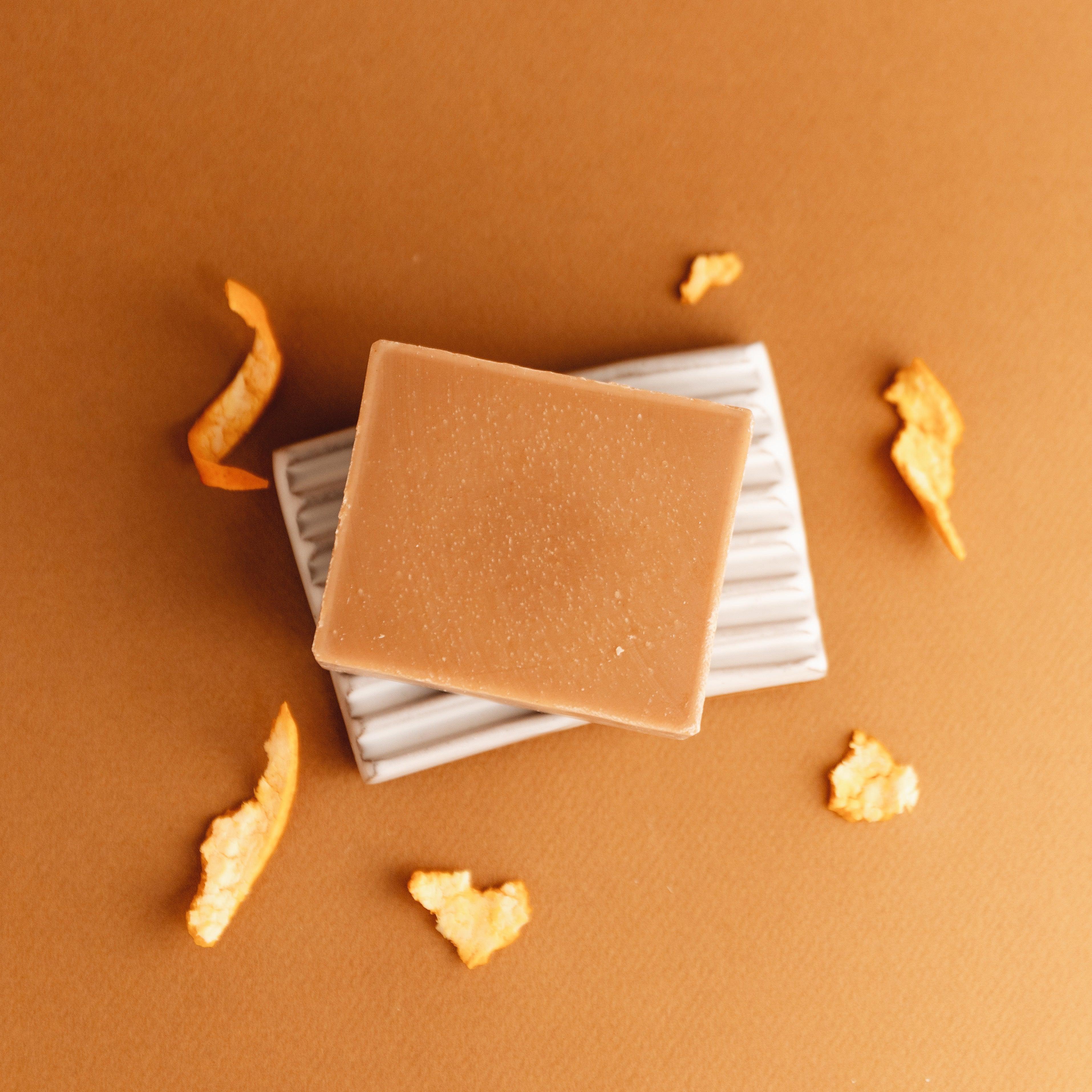 Grapefruit spearmint natural bar soap on white soap dish with orange peel on brown background