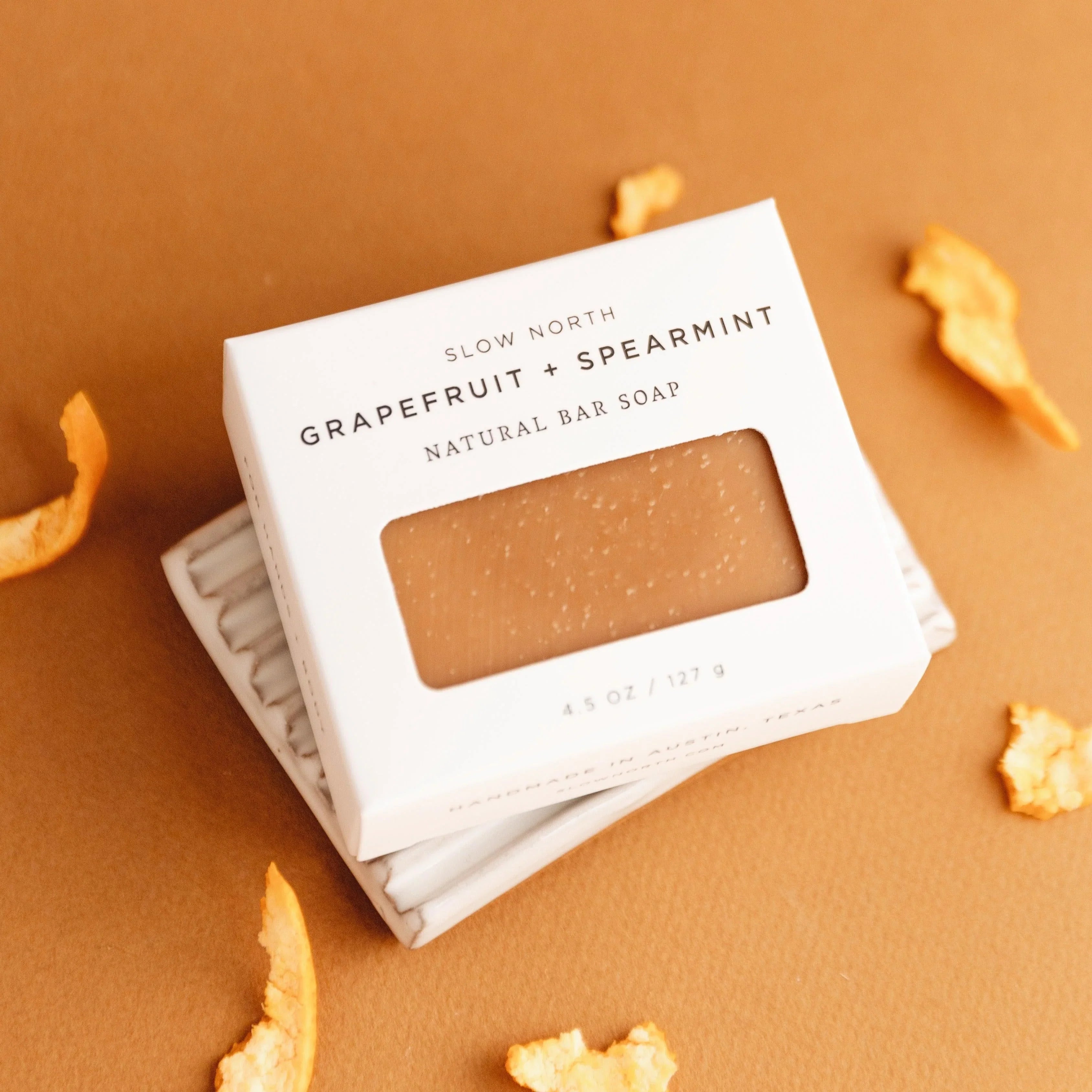 Slow North grapefruit and spearmint natural bar soap in white packaging on ceramic dish with orange peels