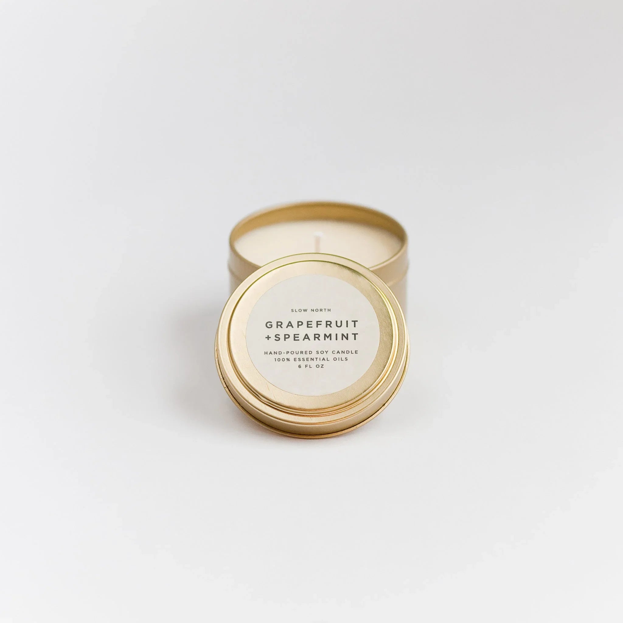 Open gold travel tin candle labeled Grapefruit + Spearmint soy candle with essential oils