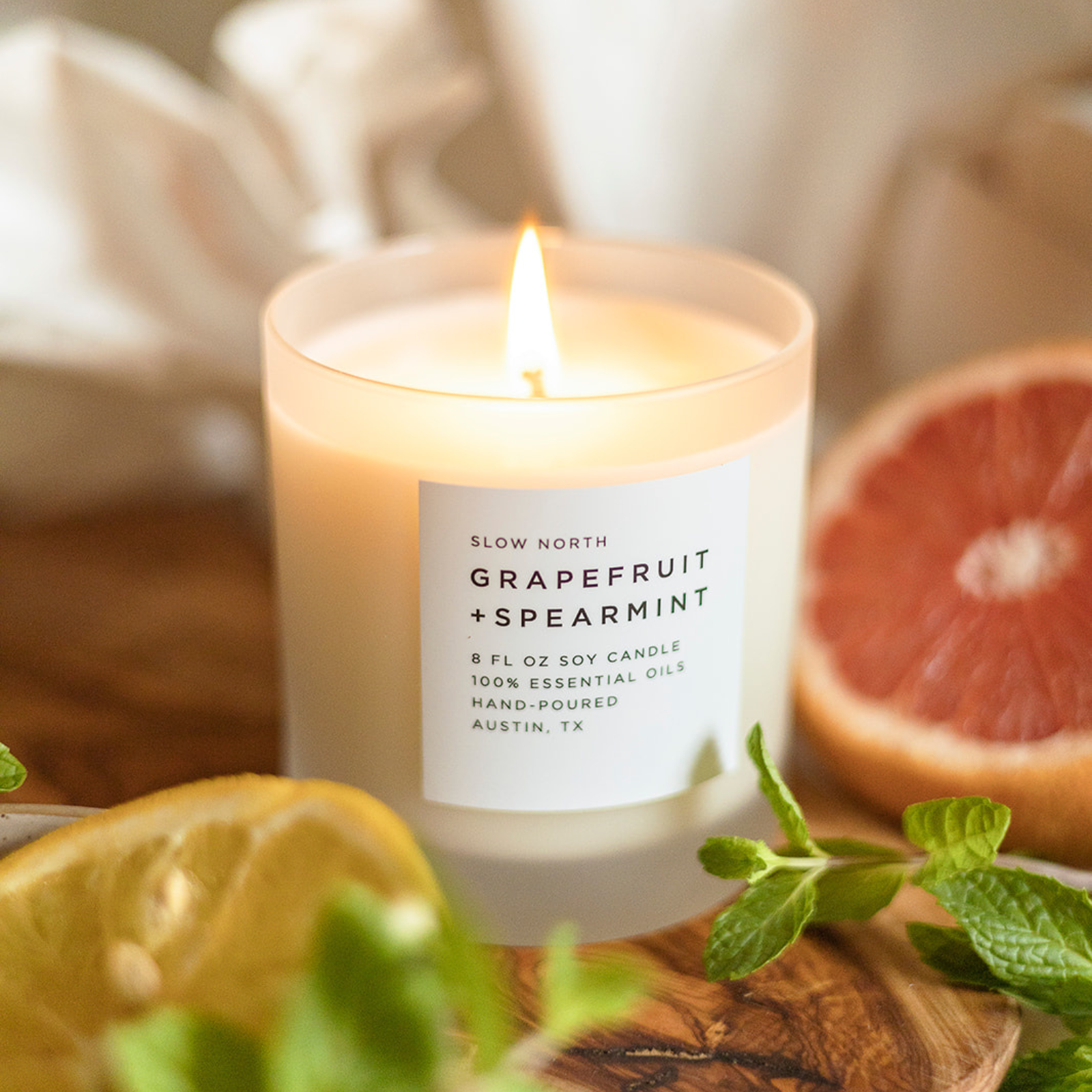 Lit Slow North grapefruit and spearmint soy candle with fresh grapefruit and mint on wooden surface