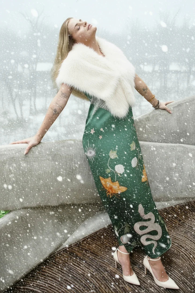 Woman in green floral maxi dress and white fur shawl posing in snowy outdoor setting